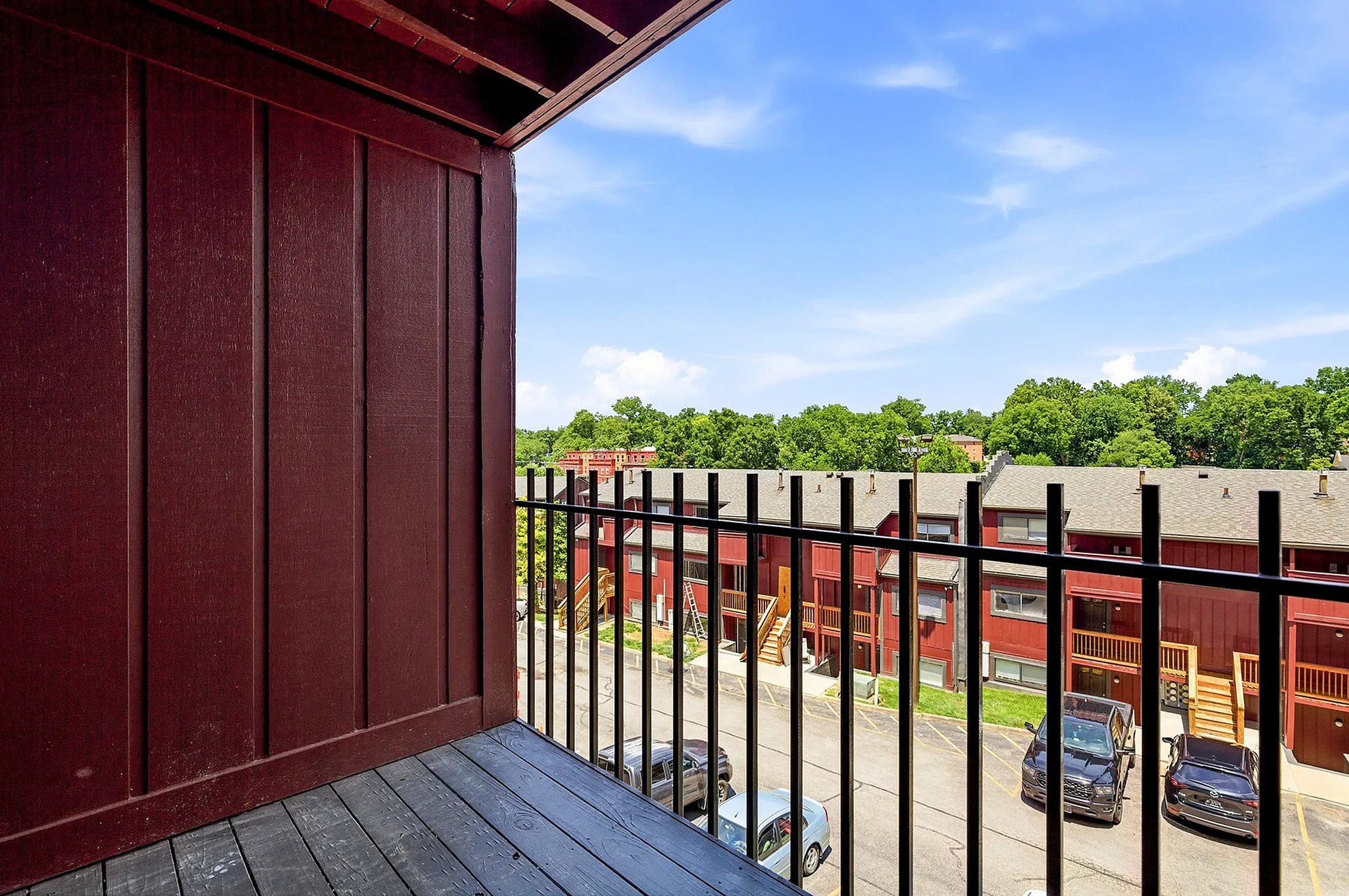 Charming view from a cozy balcony overlooking rustic buildings and lush green trees under a bright blue sky.