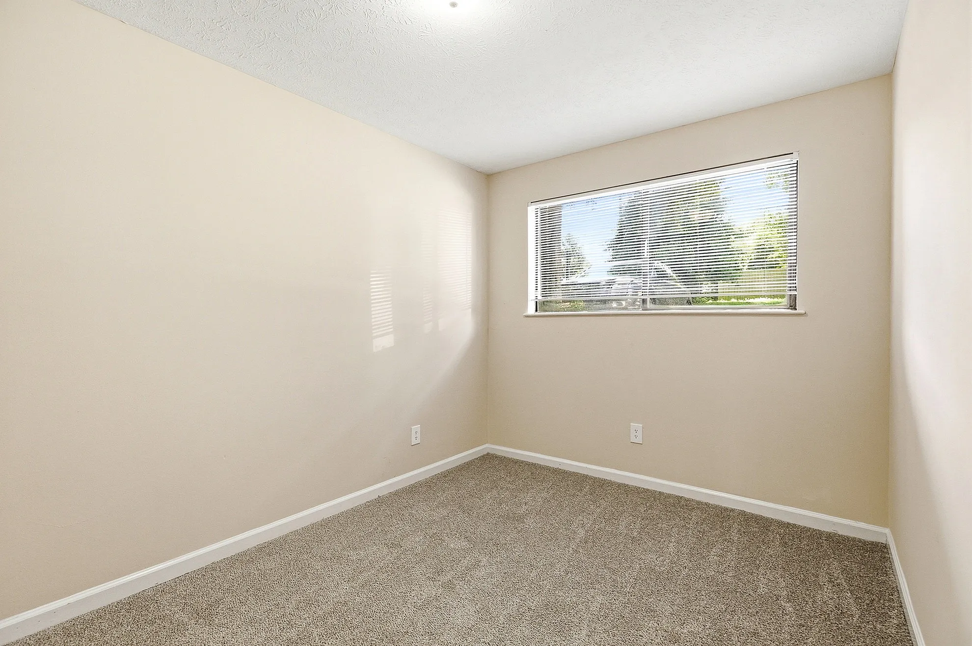 Bright and inviting bedroom with neutral walls and carpet, featuring a large window offering serene outdoor views.