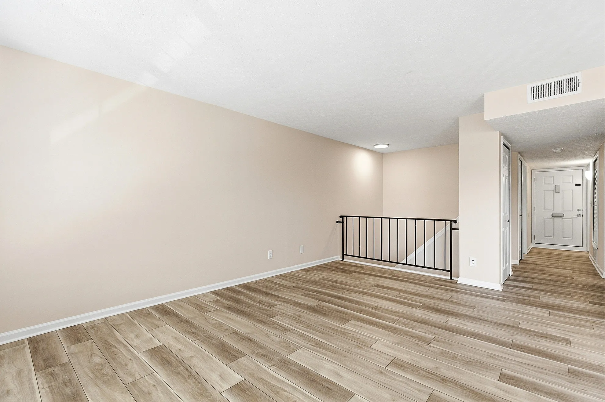 Bright and inviting hallway with modern wood flooring and a sleek railing, leading to a staircase and entrance.