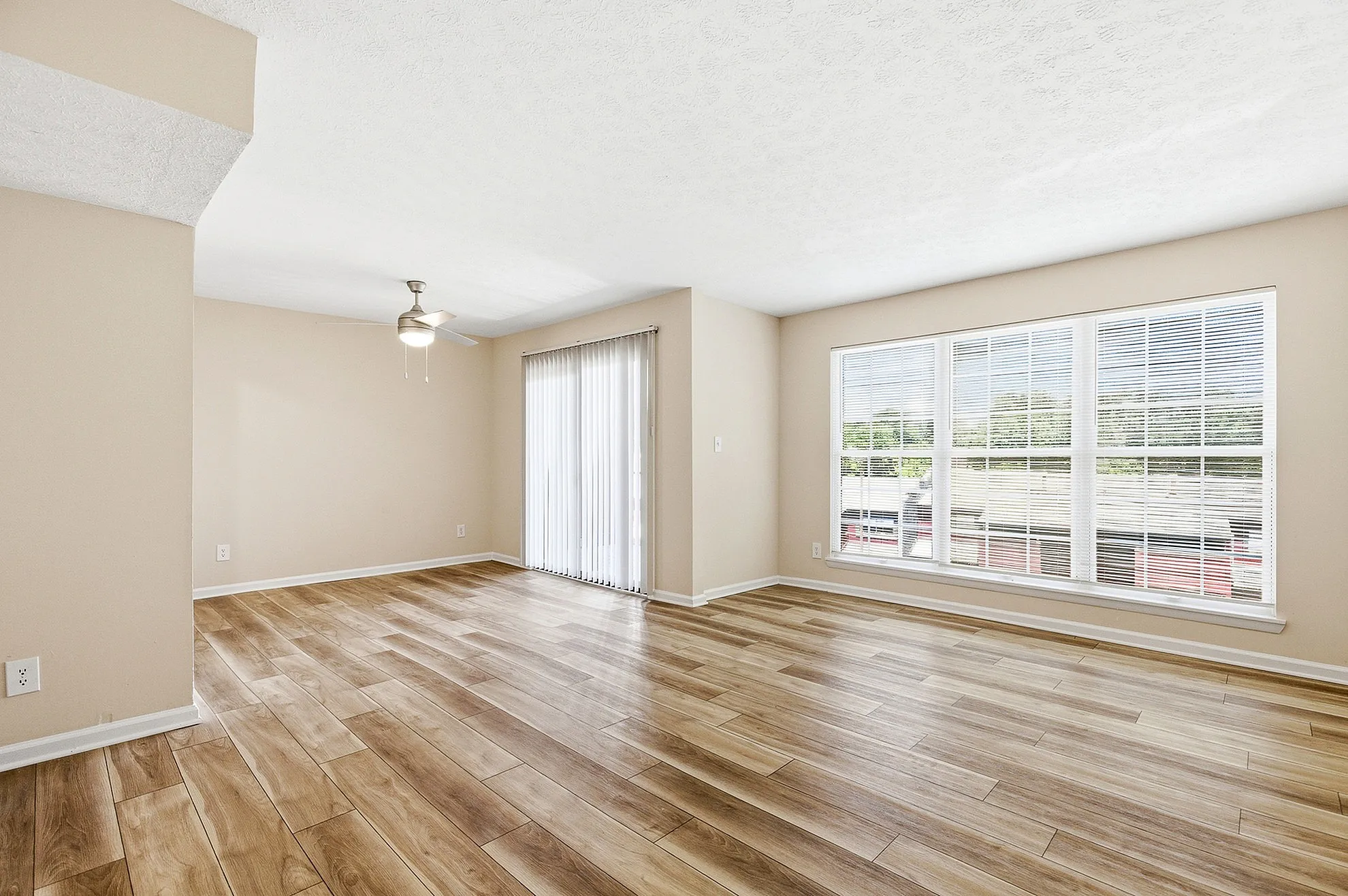 Bright and airy living room with elegant wood flooring, large windows, and contemporary ceiling fan, ideal for modern living.