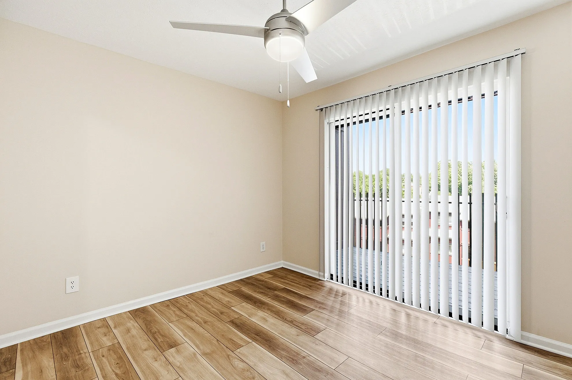 Bright room with elegant wood flooring and sliding glass doors leading to a sunlit balcony.