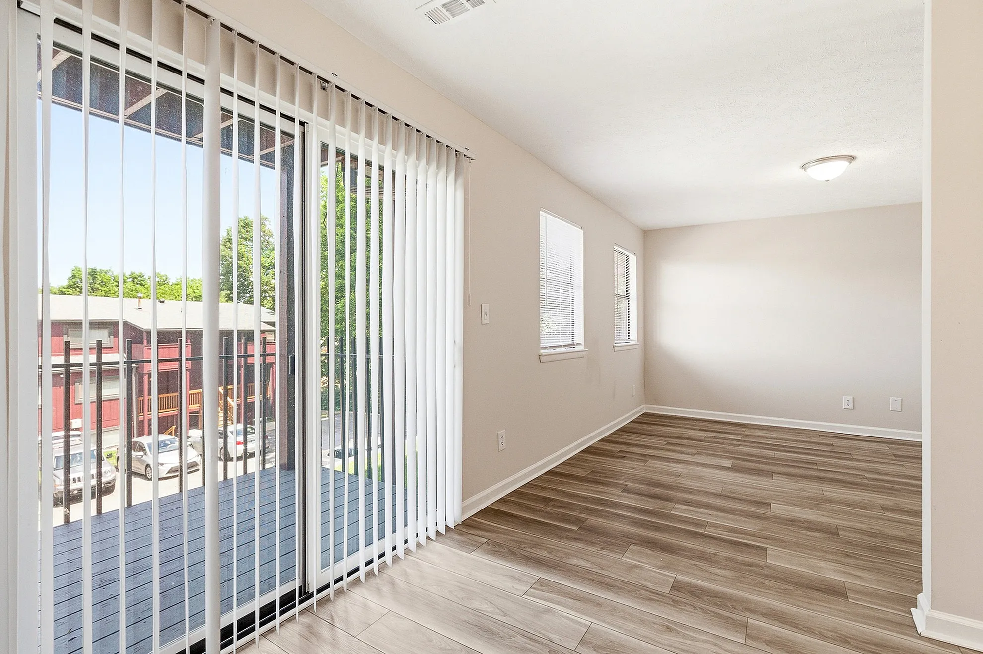Bright, modern apartment space with elegant wood flooring, large windows, and stylish vertical blinds opening to a scenic balcony view.