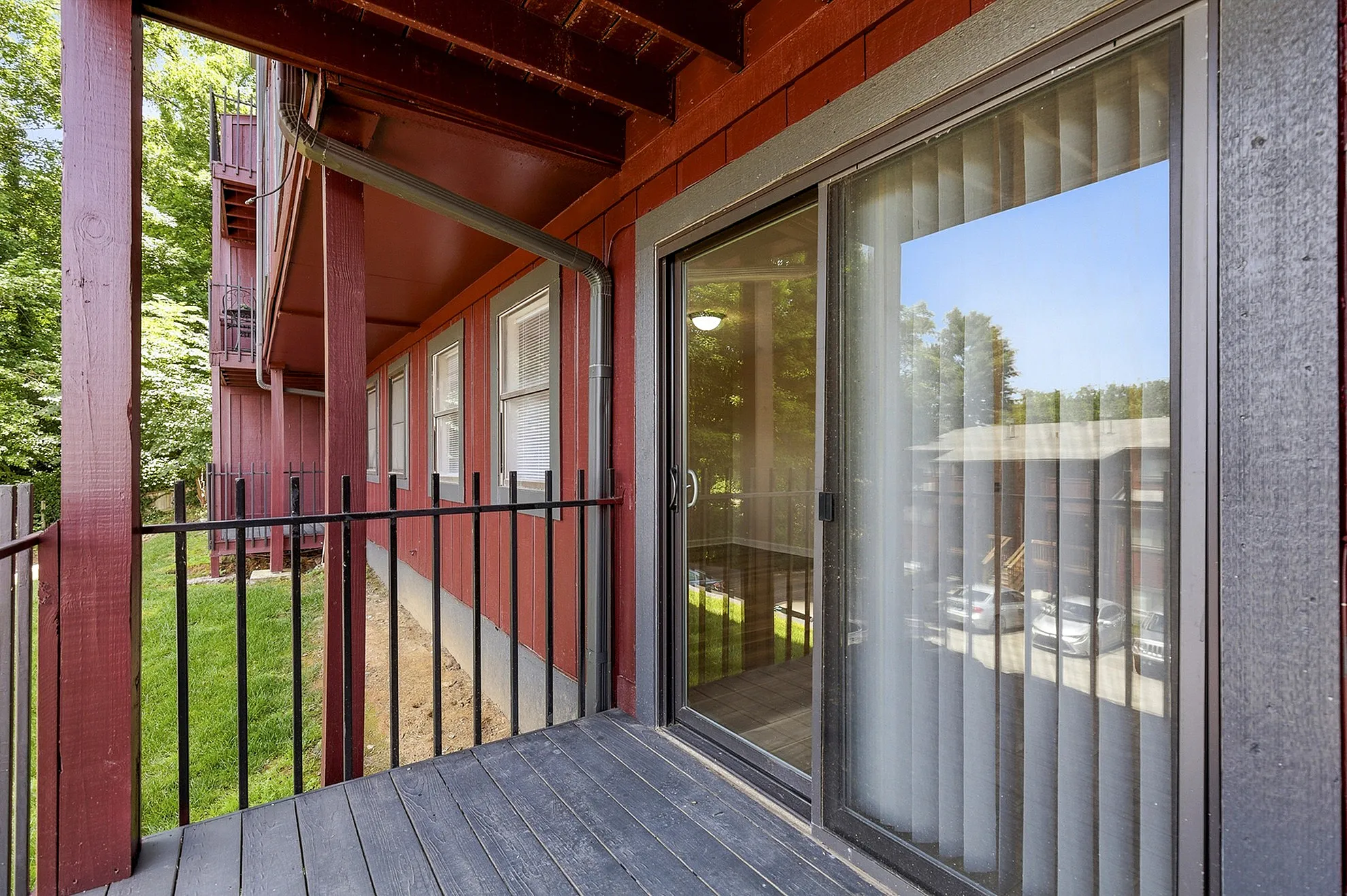 Charming apartment balcony with red wood paneling and sliding glass door, overlooking a lush green outdoor space.