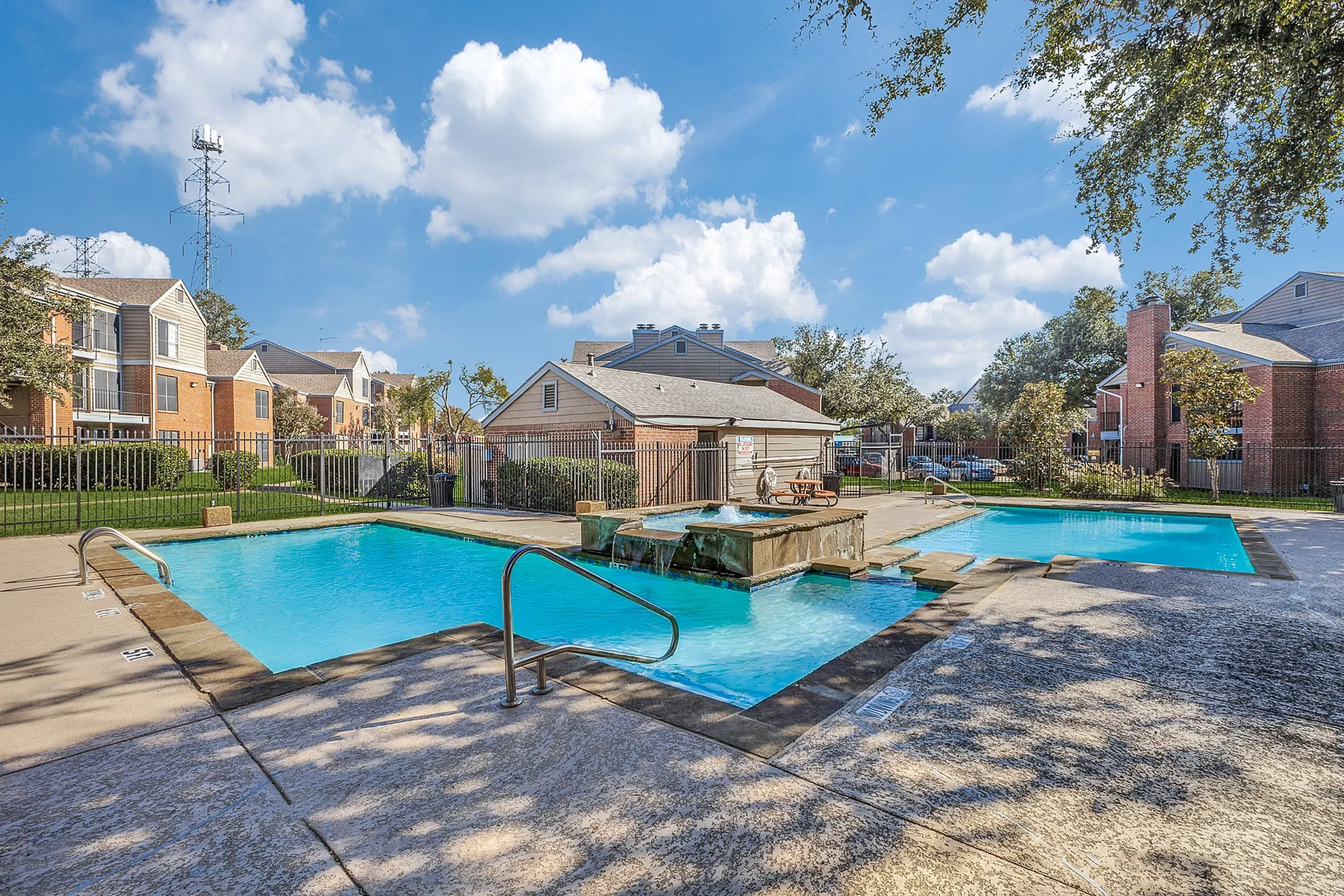 Charming apartment complex with inviting outdoor swimming pool, surrounded by lush greenery and modern brick buildings under a clear blue sky.