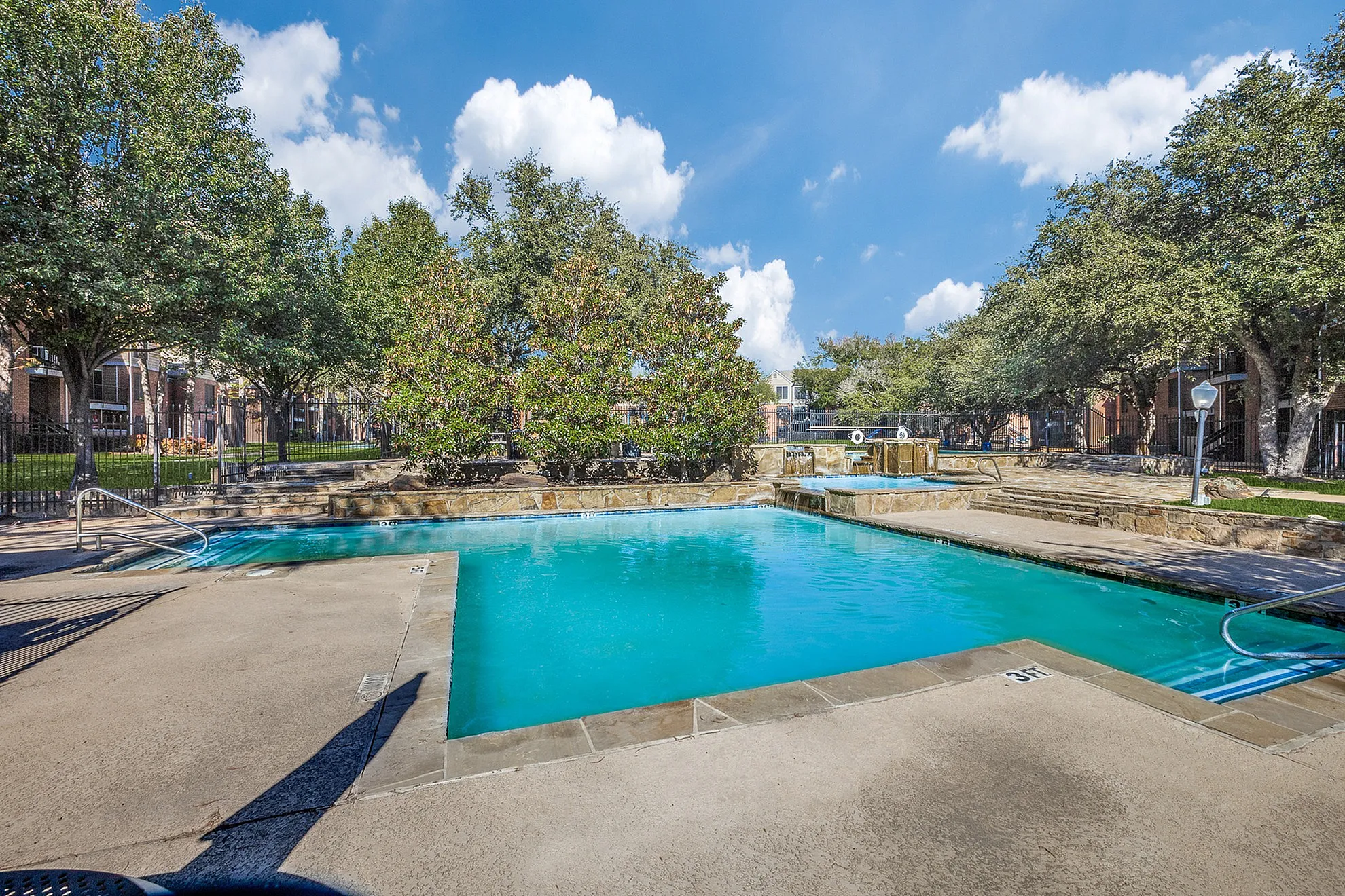 Inviting outdoor pool area surrounded by lush greenery and serene blue skies, perfect for relaxing and enjoying the sun.