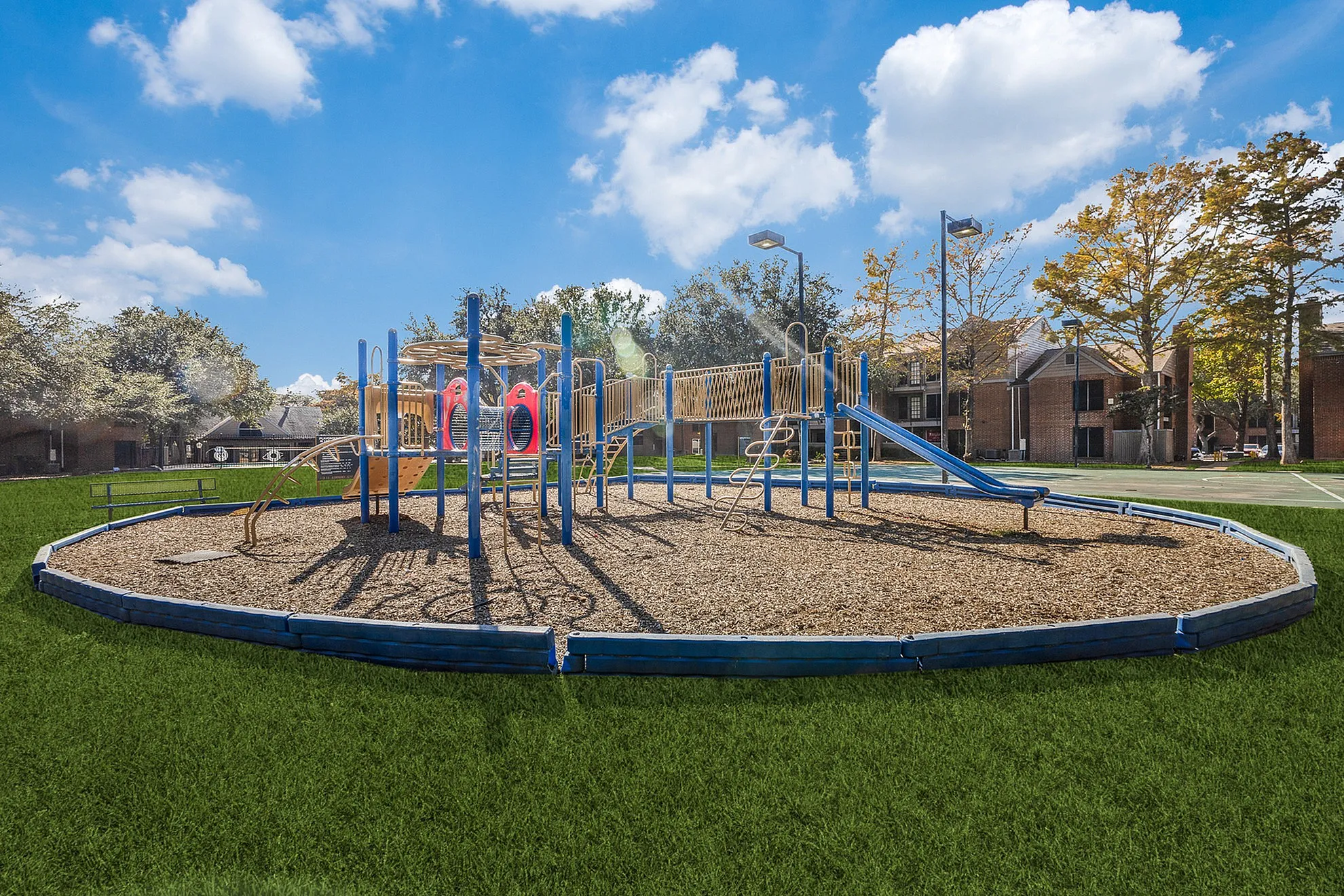 Lively playground featuring colorful climbing structures and slides, set in a green park under a bright blue sky.