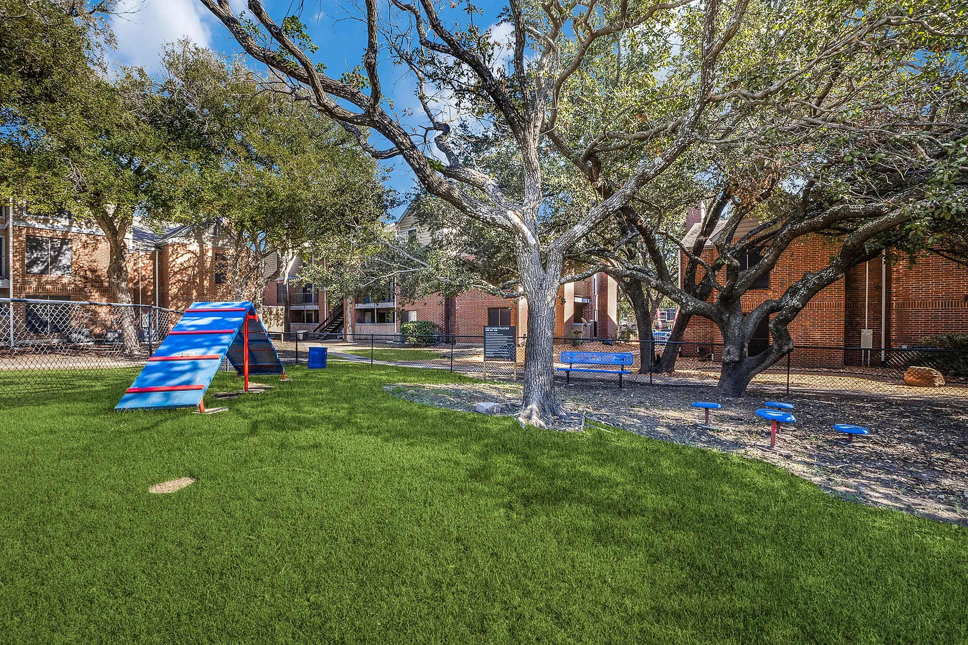 Charming apartment exterior with a lush green dog park, agility equipment, and serene surroundings, perfect for pet lovers.