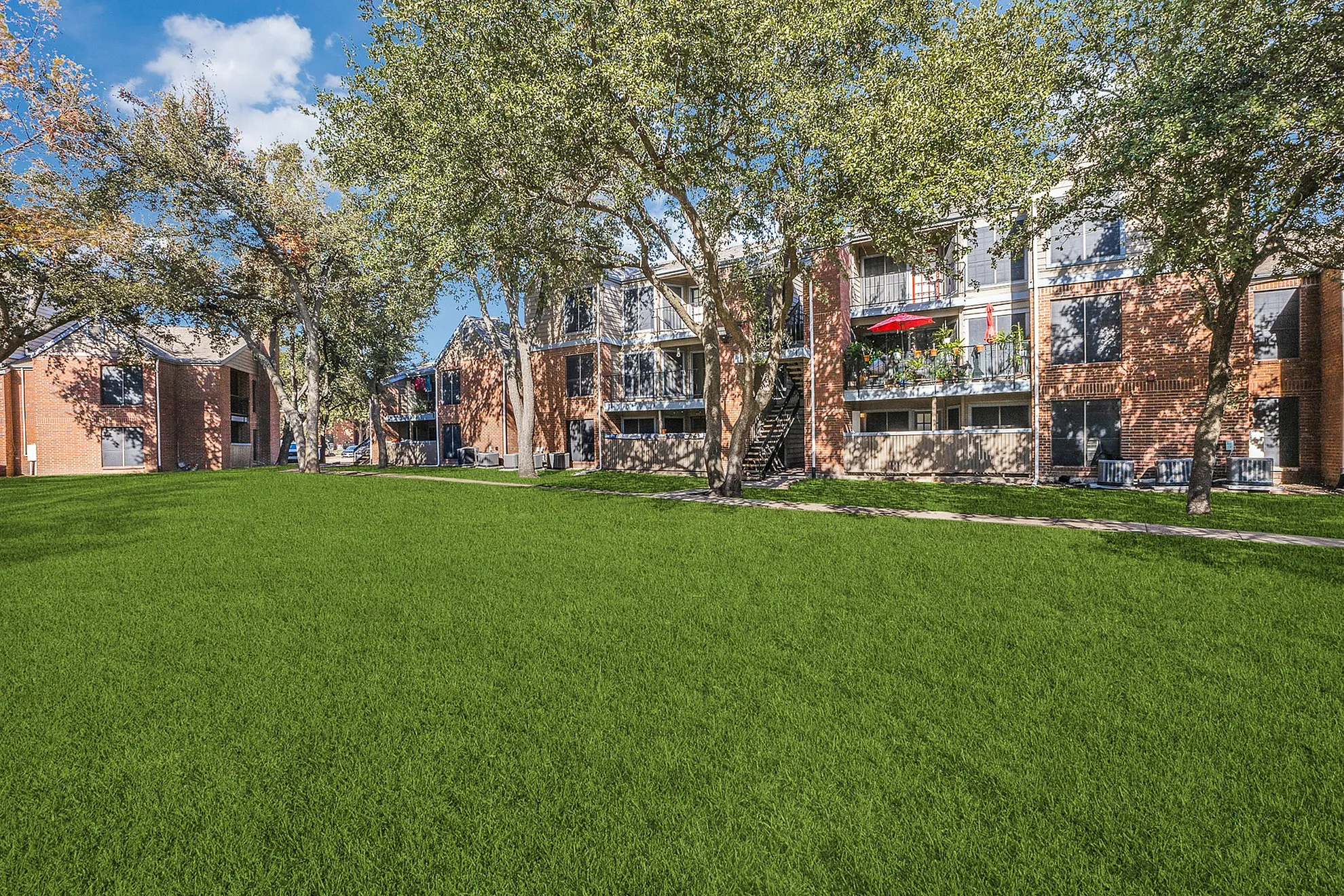 Charming apartment complex with brick facade, lush green lawn, and inviting balconies.