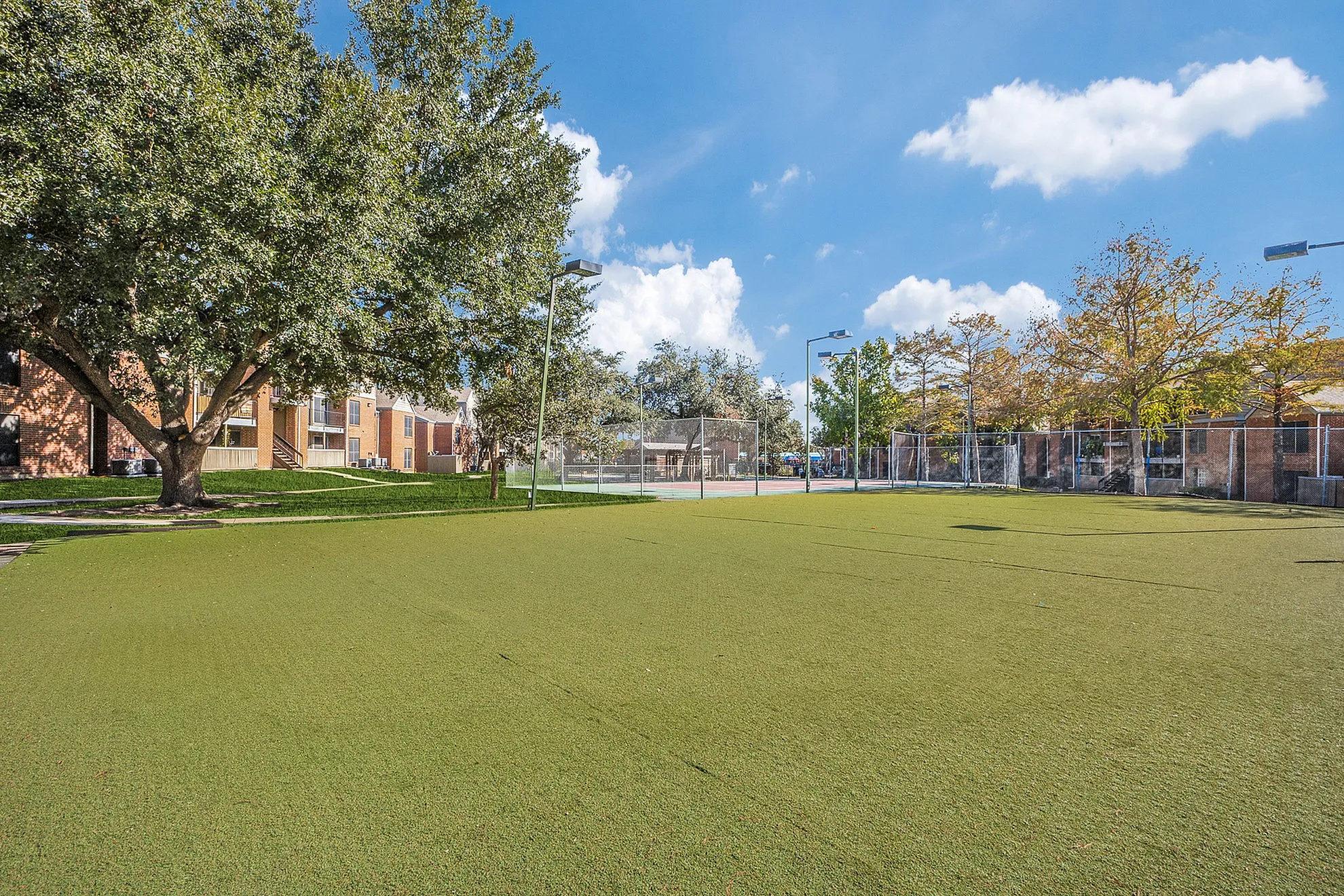Expansive green courtyard with lush trees and modern fencing, offering a serene outdoor space for relaxation and activities.