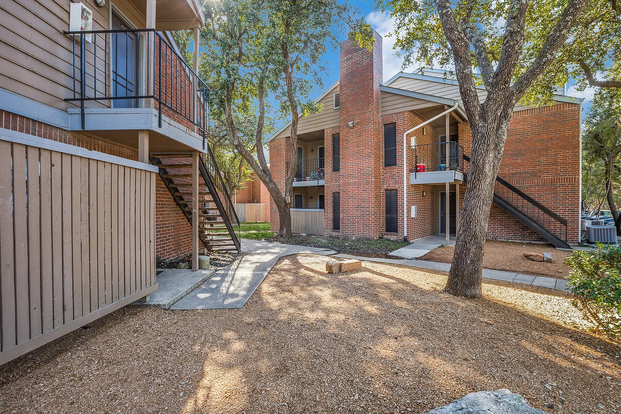 Charming brick apartment building with shaded walkways and inviting outdoor spaces.