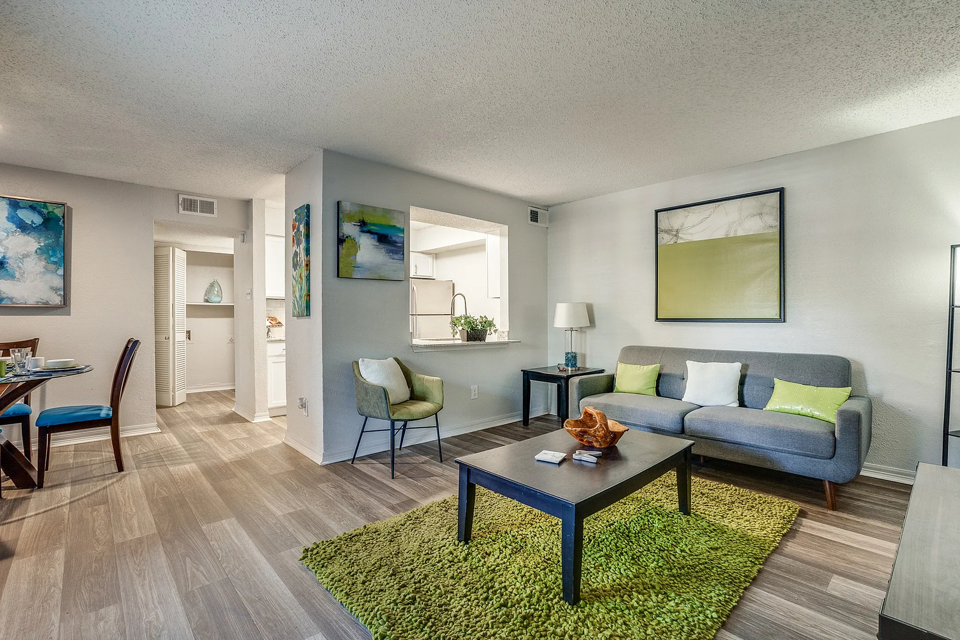 Modern living room with elegant decor, featuring a cozy gray sofa, vibrant green rug, and stylish dining area with abstract art on the walls.