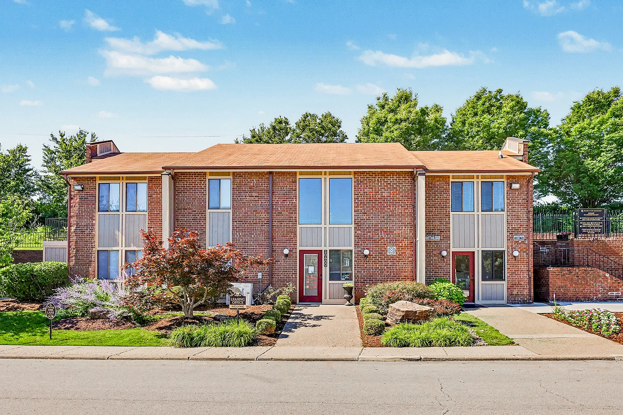 Charming brick apartment building with lush landscaping and modern design, offering a welcoming community atmosphere.