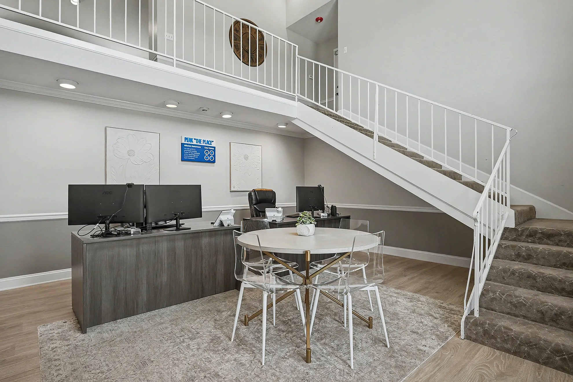 Modern apartment lobby with sleek wooden flooring, stylish desk setup, and elegant staircase leading to the upper level.