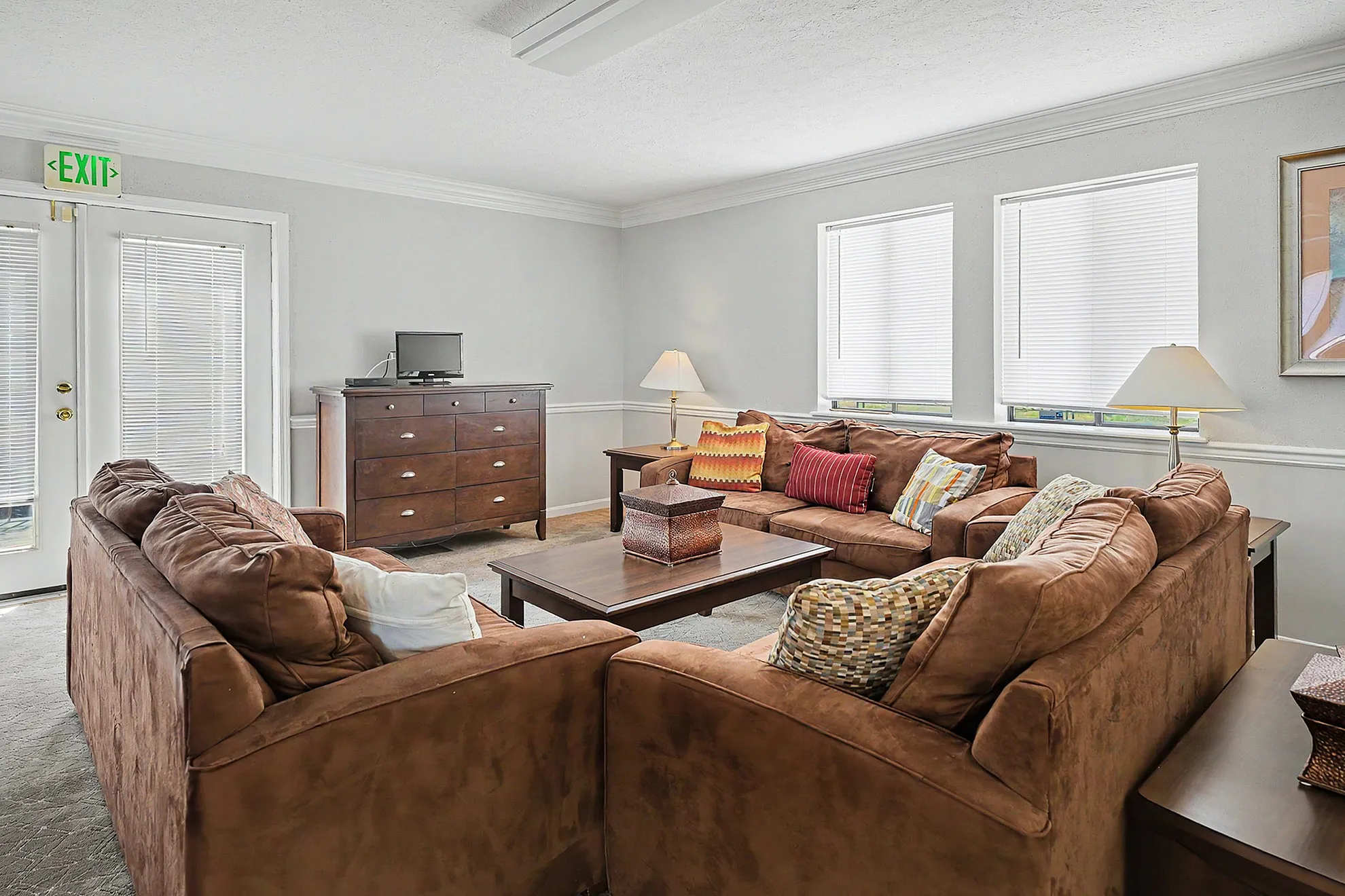 Inviting living room with plush brown sofas, vibrant throw pillows, and ample natural light through large windows.