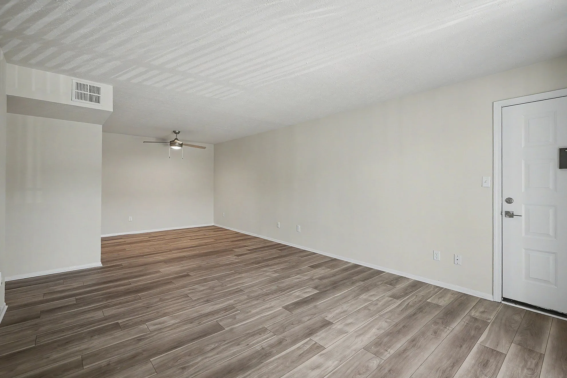 Spacious living area with elegant wood-style flooring, modern ceiling fan, and abundant natural light, perfect for relaxation.