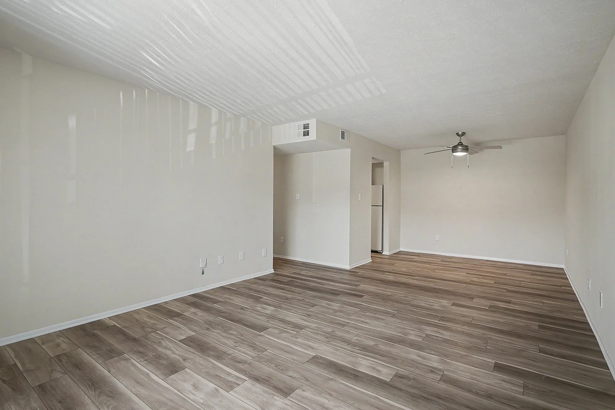 Bright and spacious living area with elegant wood flooring, neutral walls, and a modern ceiling fan, designed for comfort and style.