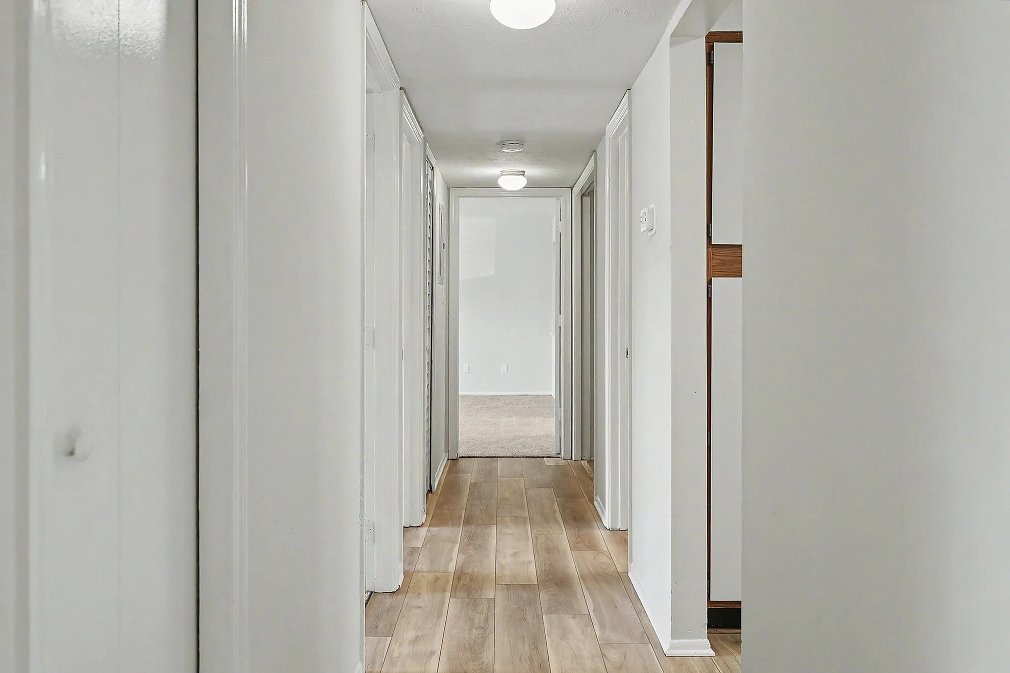 Bright hallway with modern wooden flooring and sleek white walls, leading to spacious rooms.