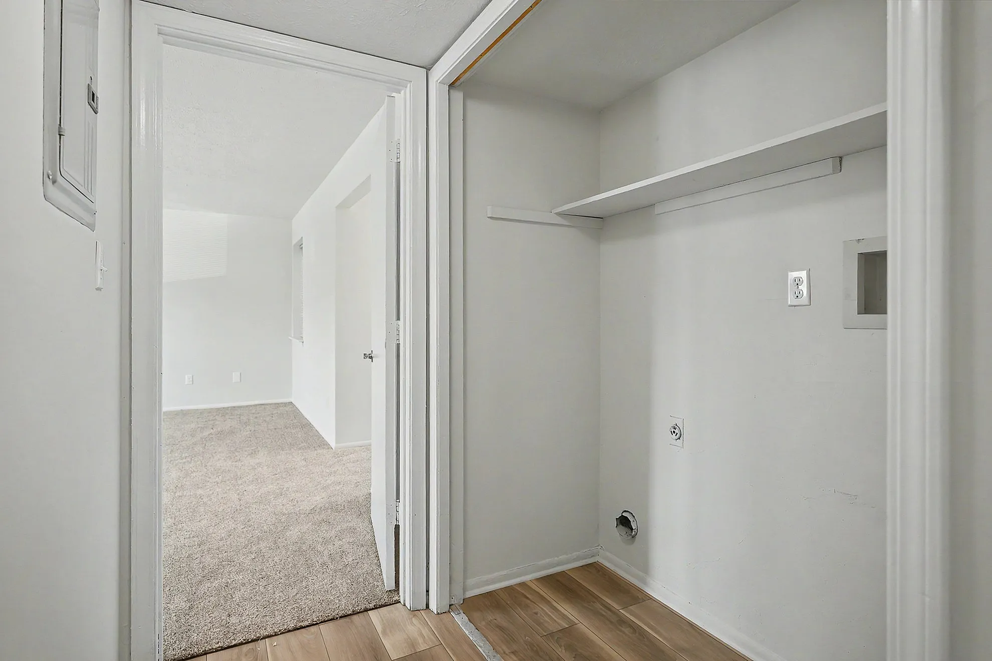 Bright hallway with a cozy carpeted room visible, elegant wooden flooring, and a convenient laundry hookup area.