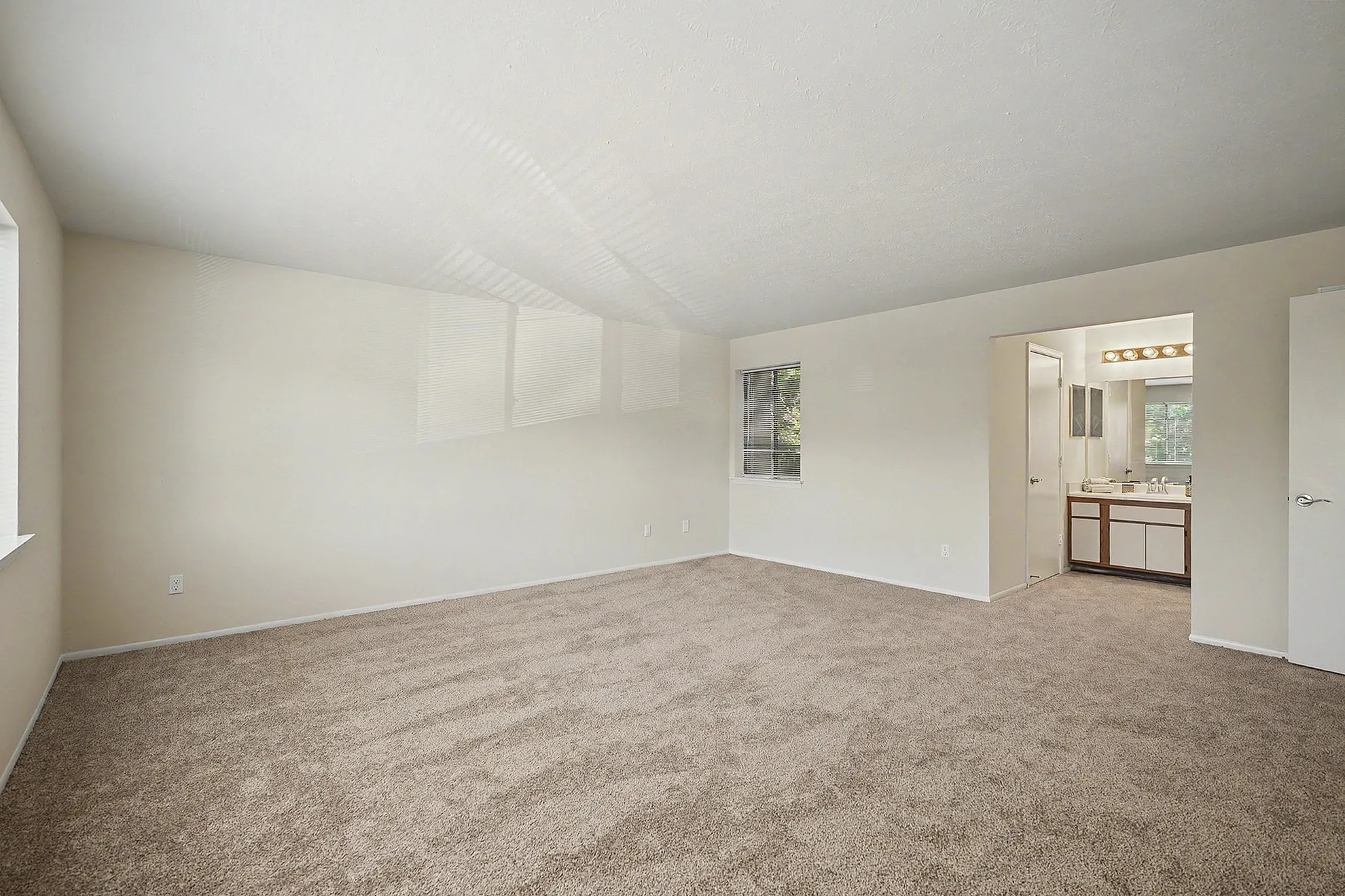 Bright, spacious bedroom with plush carpet and en-suite bathroom, featuring large windows for natural light.