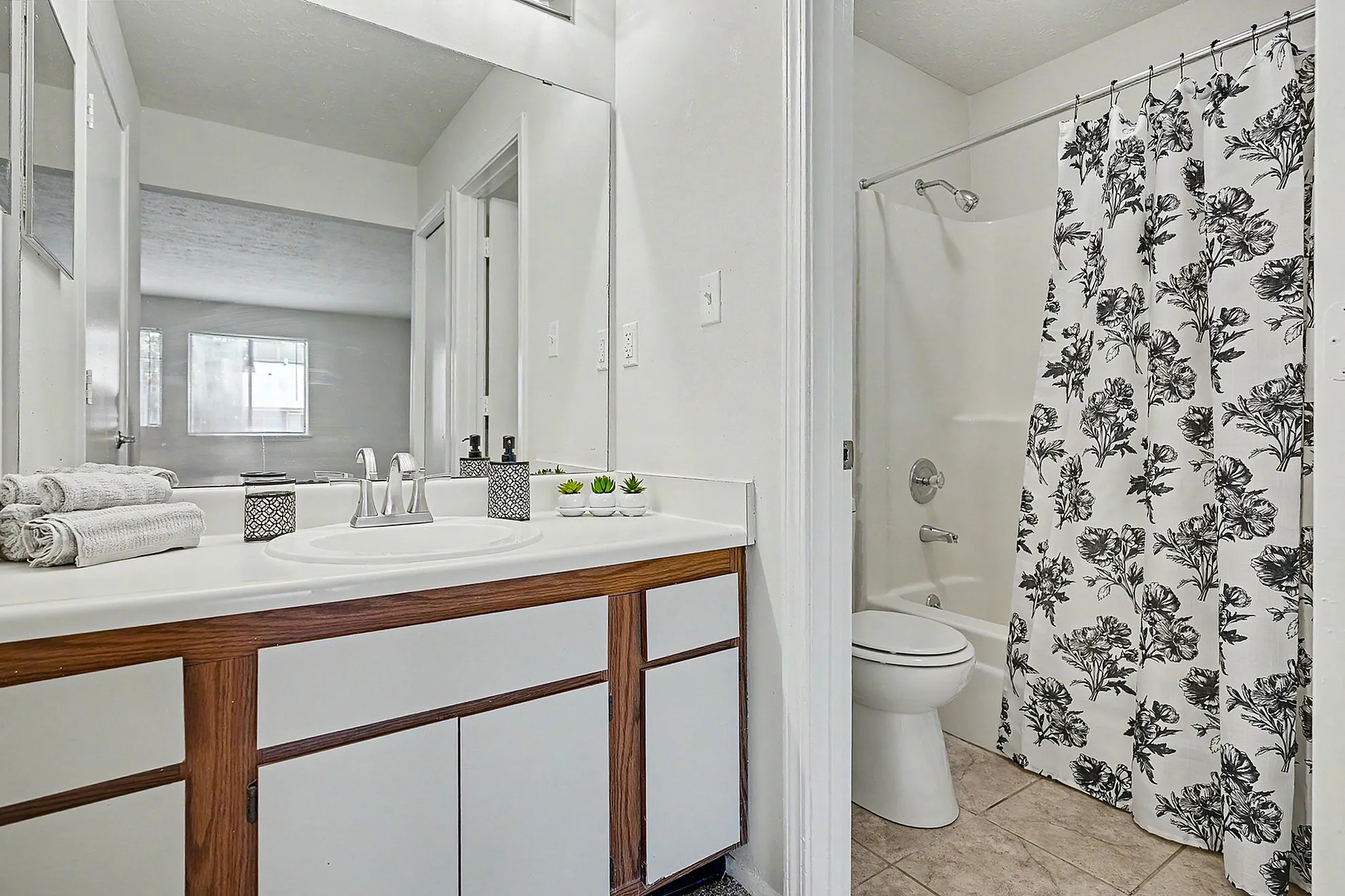 Elegant bathroom featuring a modern vanity with sleek faucets, decorative accents, and a floral shower curtain for a stylish touch.