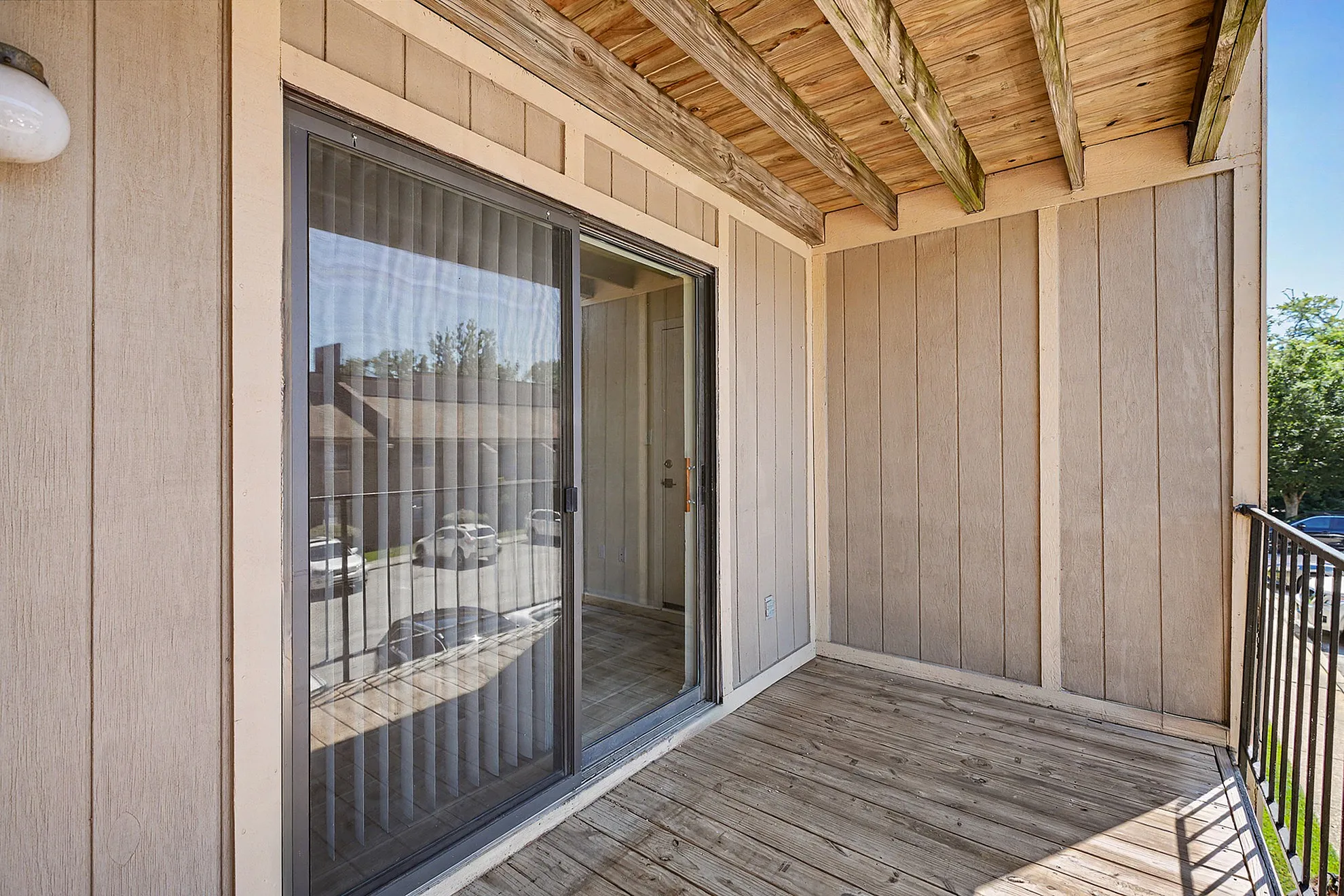 Inviting apartment balcony with wooden decking and glass sliding door offering a serene outdoor escape.