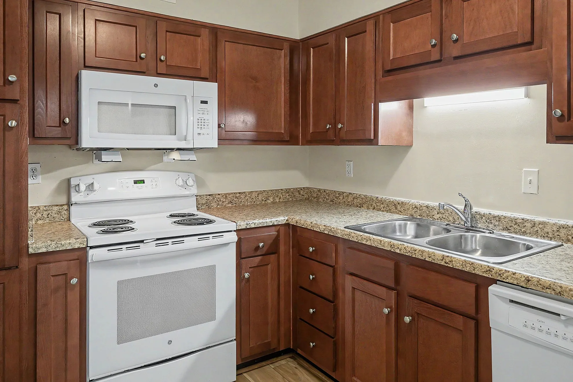 Modern kitchen with elegant wooden cabinetry, granite countertops, and sleek stainless steel sink, featuring a white stove and microwave for a polished look.