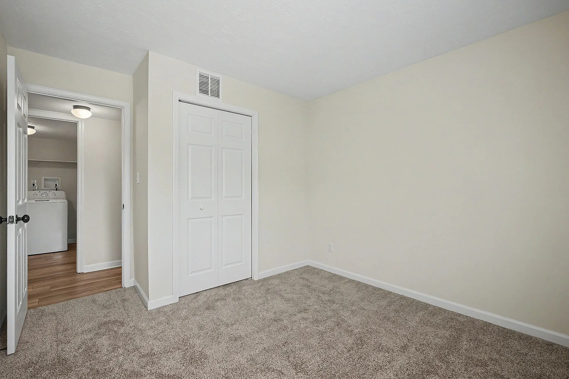 Bright bedroom with soft carpet, fresh paint, and convenient access to laundry room, ideal for modern living.