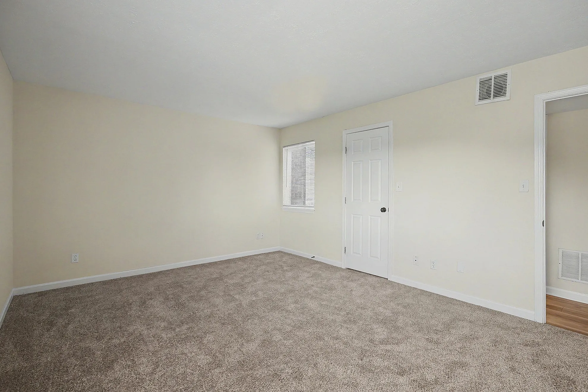 Spacious bedroom with plush carpet, neutral walls, and abundant natural light from a large window.