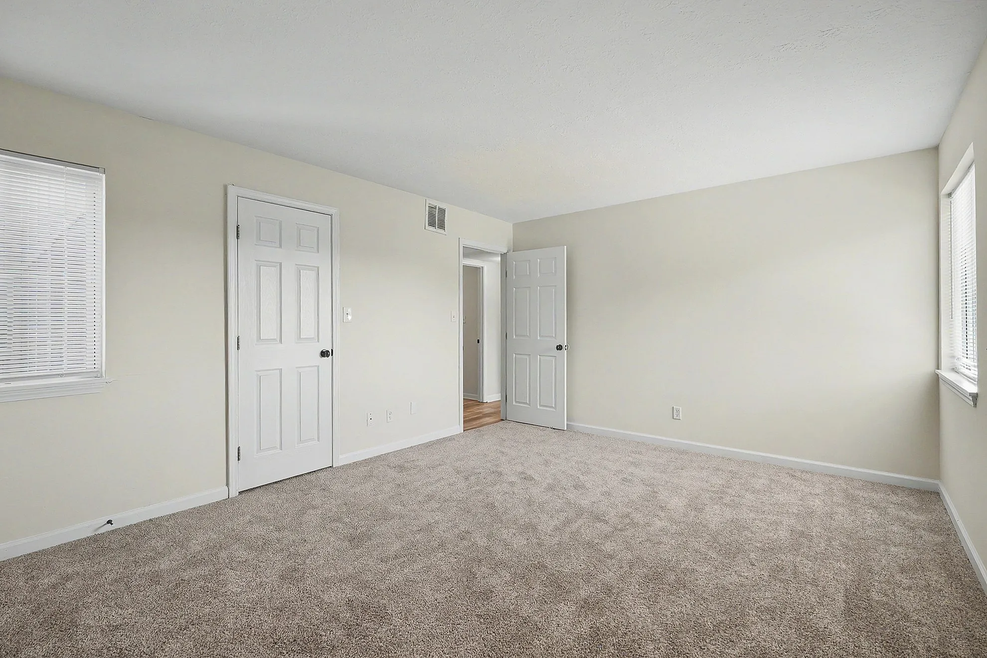 Bright and spacious bedroom featuring plush carpeting and abundant natural light through large windows.