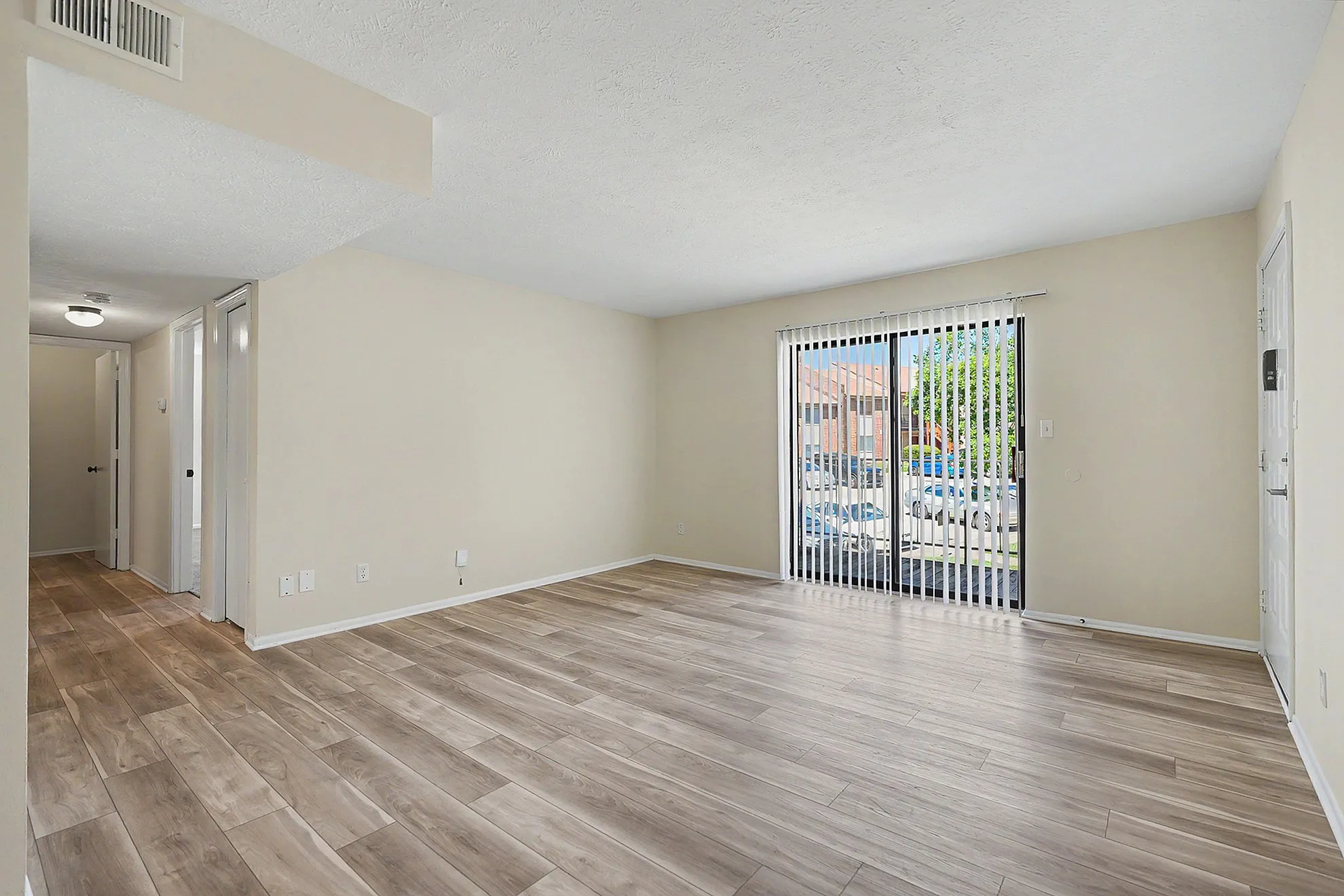 Bright and spacious living room with elegant wood-style flooring and large sliding glass doors opening to a scenic outdoor view.