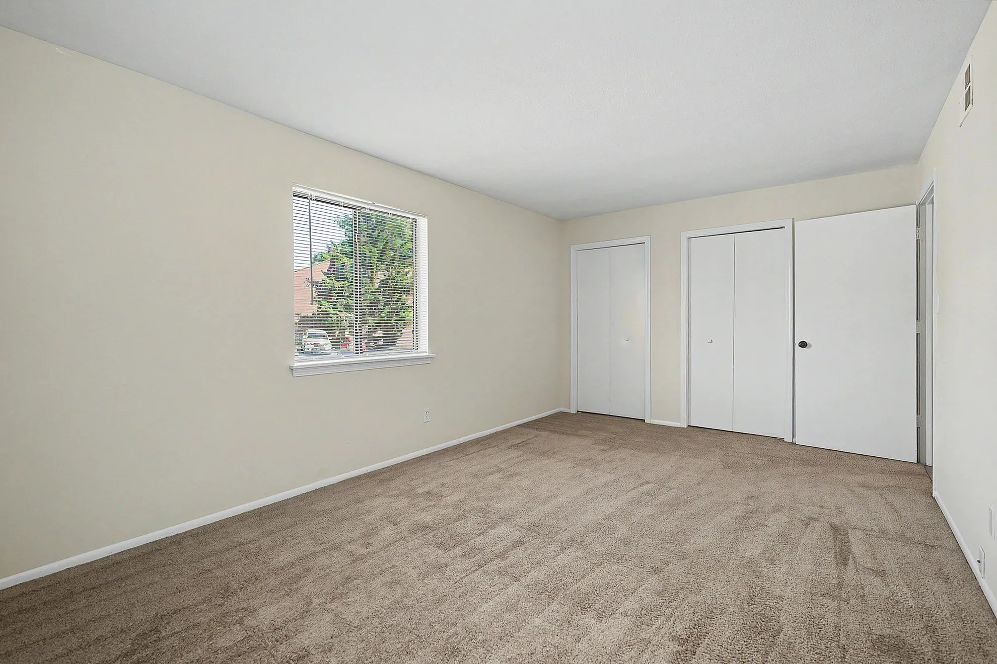 Bright and airy bedroom with plush carpeting, ample closet space, and a large window offering a serene view.