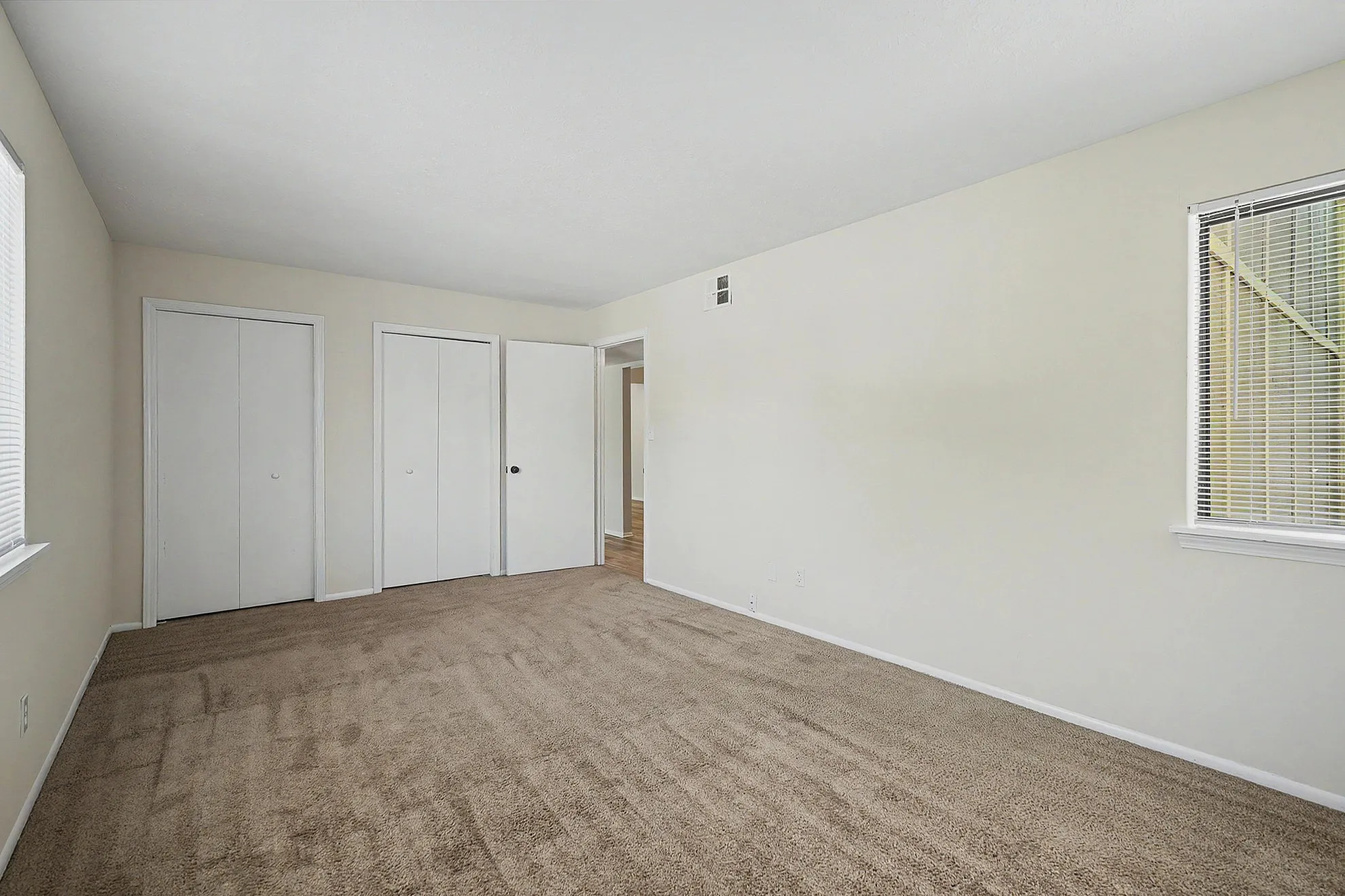 Spacious room with plush carpet, abundant natural light, and dual white closet doors perfect for comfortable living.