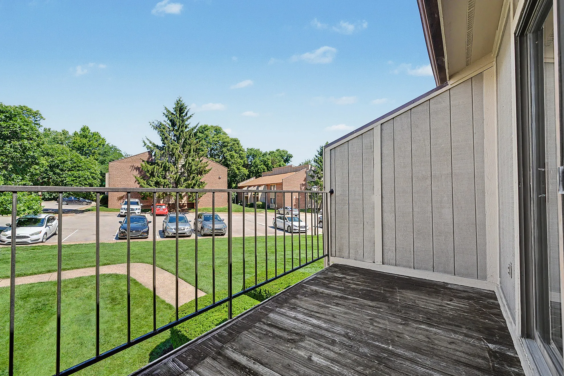 Inviting apartment balcony overlooking a lush green garden and nearby residential buildings, perfect for relaxation and enjoying the serene views.