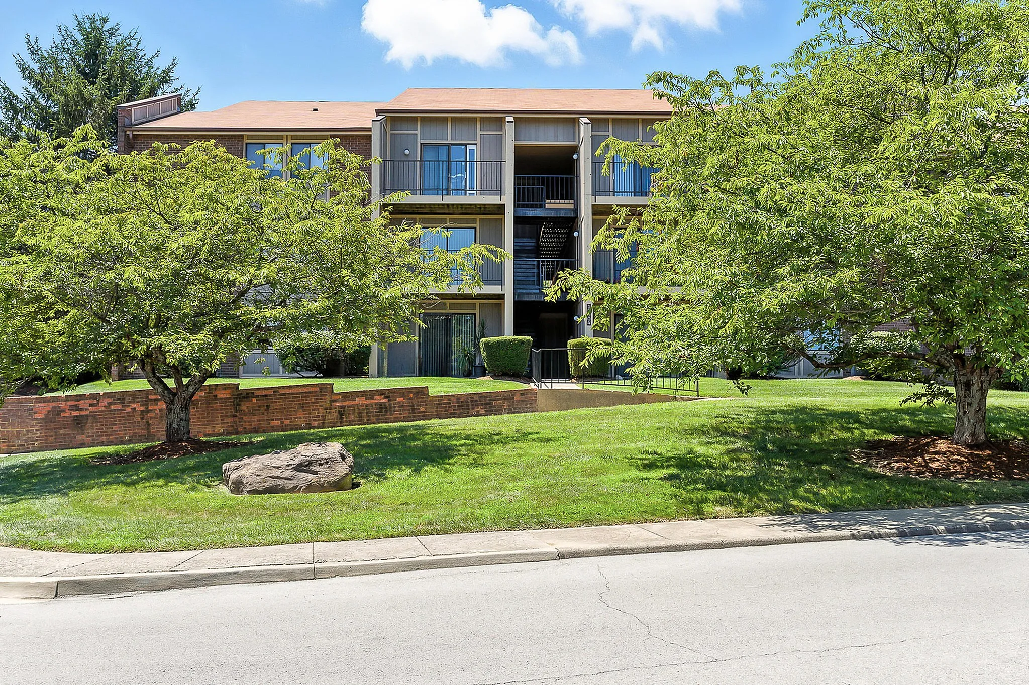 Charming apartment complex surrounded by lush greenery and mature trees, offering a serene and welcoming atmosphere.