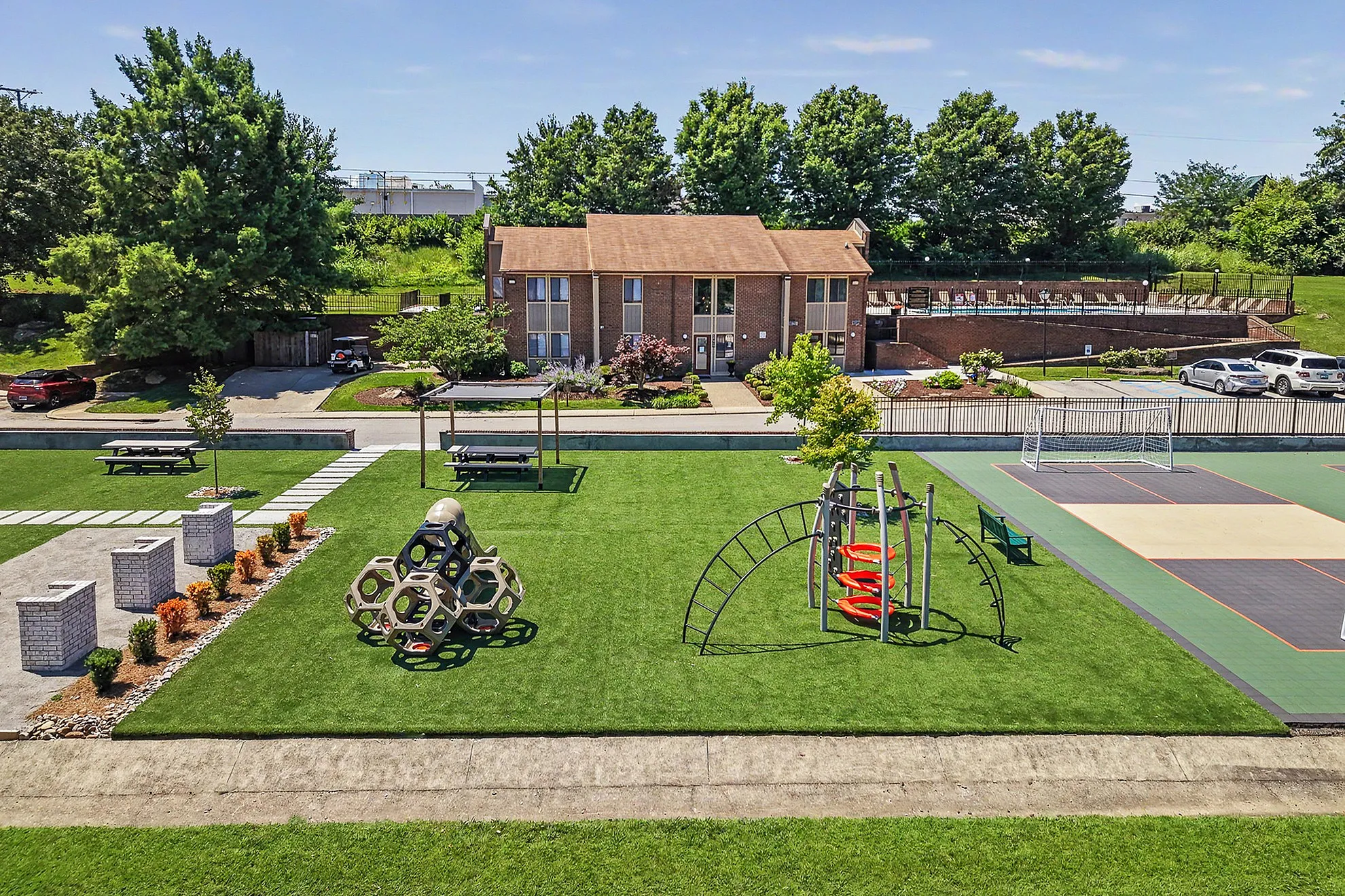 Inviting apartment complex surrounded by lush greenery, featuring a modern playground, picnic benches, and a well-maintained sports court.