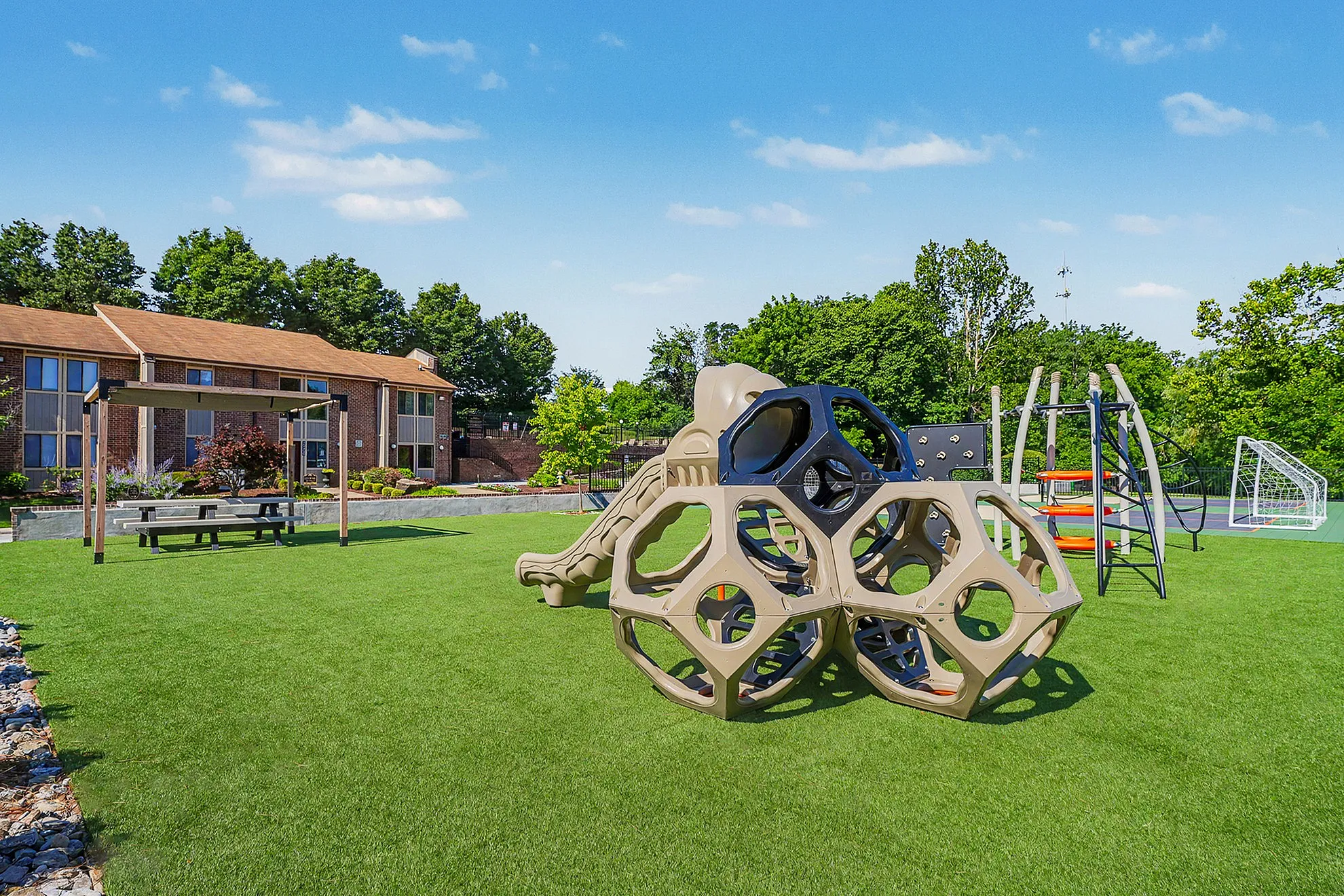 Inviting outdoor playground area with modern climbing structures, lush green lawn, and adjacent brick apartment exteriors.