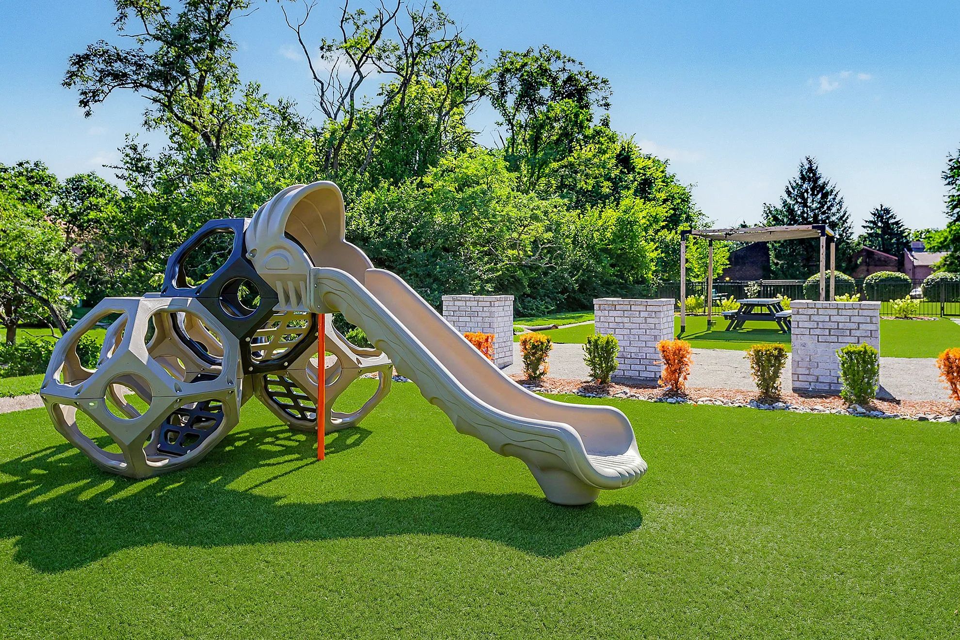 Inviting playground with modern slide and geometric climbing structure surrounded by lush greenery and picnic area, perfect for family fun.
