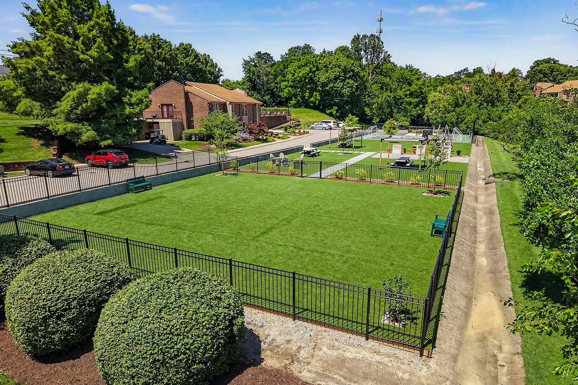 Vibrant community park featuring lush green lawns, a fenced area for activities, and inviting picnic spots, surrounded by serene natural beauty and modern homes.