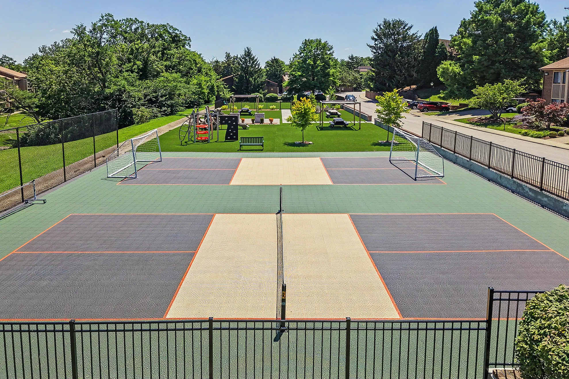 Vibrant outdoor sports and recreation area featuring a multi-purpose court, soccer goals, and a lush playground surrounded by greenery.