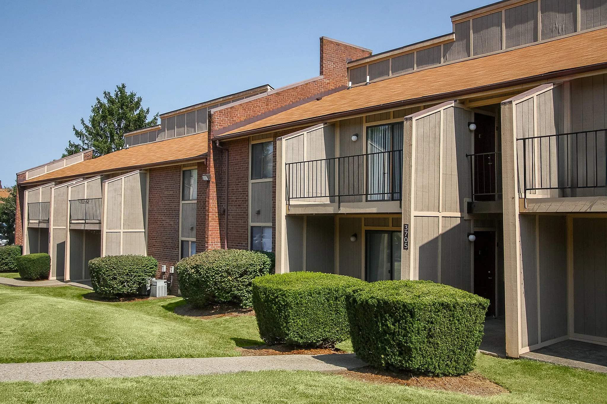 Charming apartment complex with modern balconies, set against a backdrop of lush greenery and a clear blue sky.