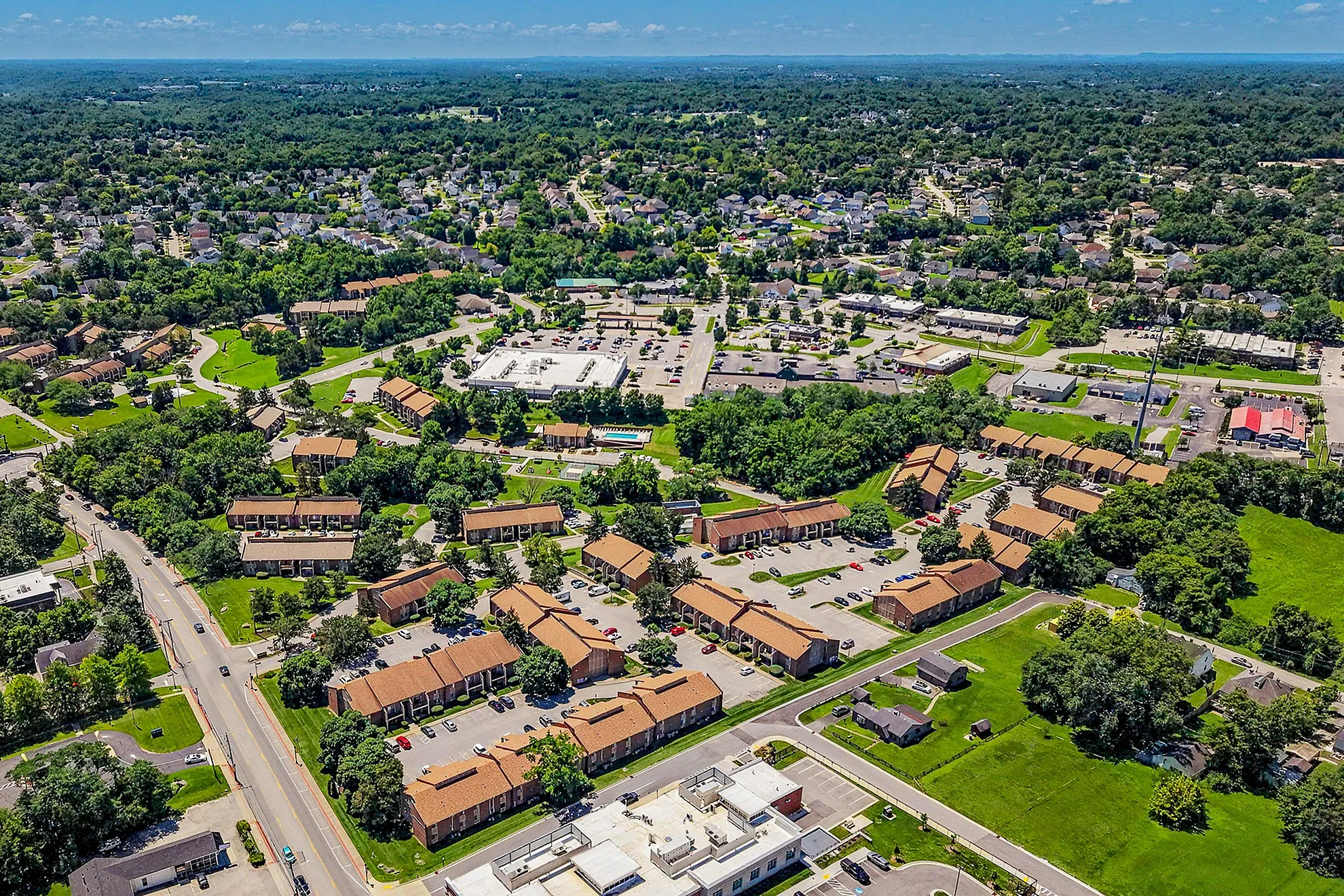 Vibrant aerial view of a lush suburban community with spacious apartments, ample parking, and beautifully landscaped green spaces.