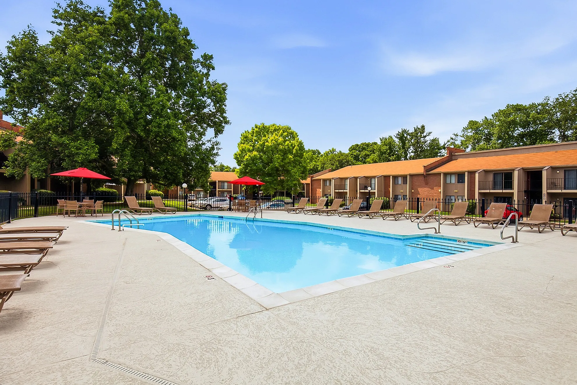 Inviting community swimming pool surrounded by sun loungers and lush green trees, perfect for a relaxing day outdoors.