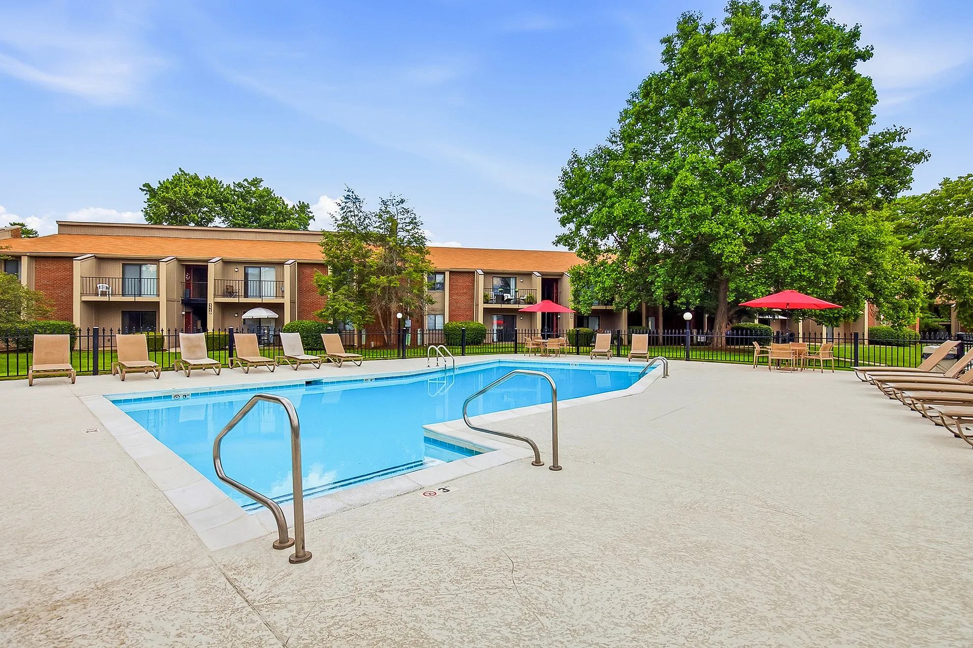 Inviting apartment complex with sparkling swimming pool, sun loungers, and lush greenery, perfect for relaxation and leisure.