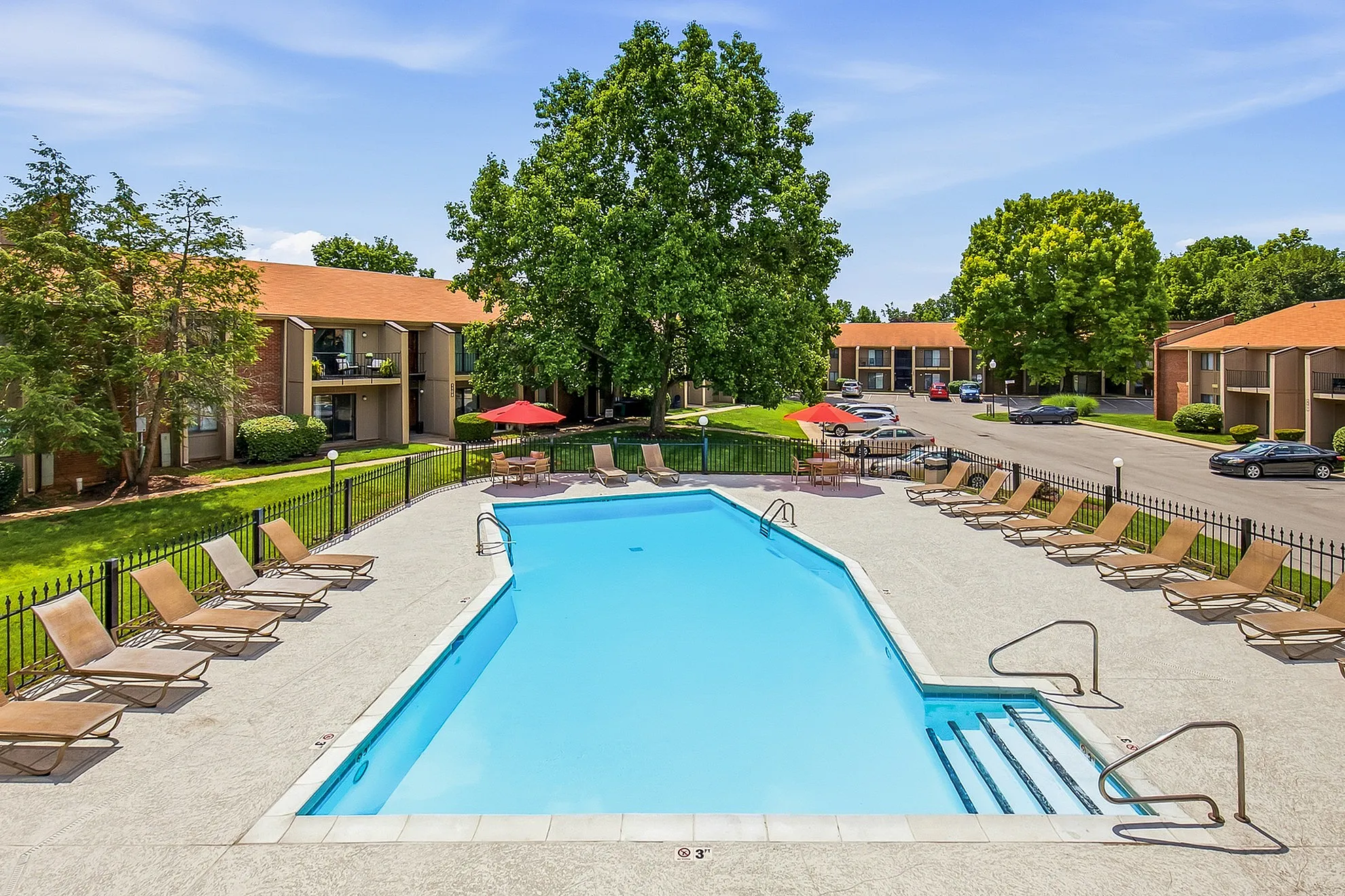 Inviting pool area surrounded by comfortable lounge chairs, set against the backdrop of charming apartment buildings and lush greenery.