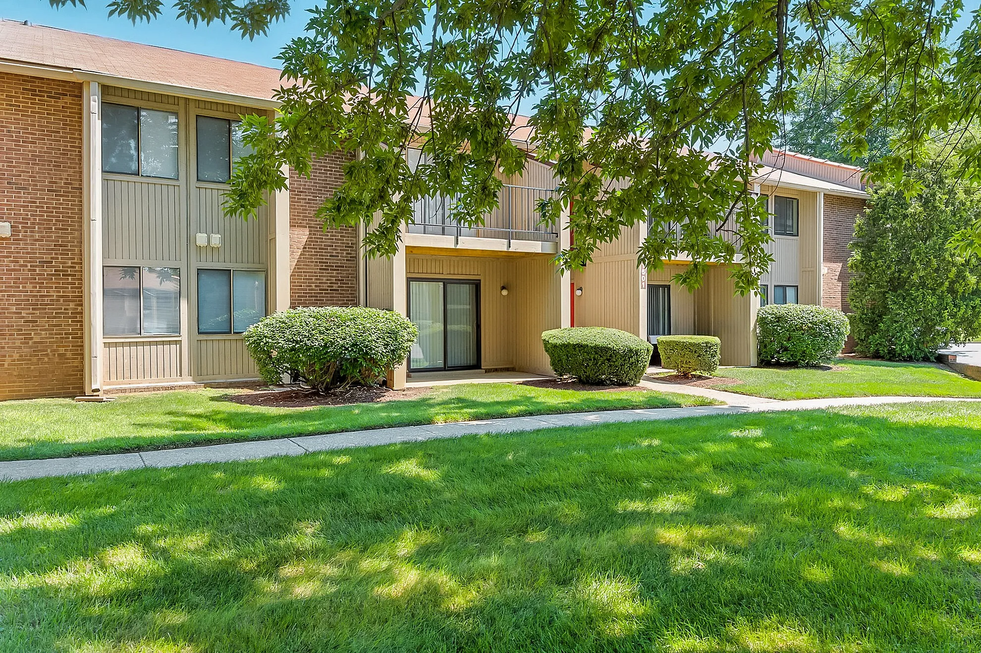 Charming apartment complex exterior with lush green landscaping and modern architecture, inviting atmosphere for residents.