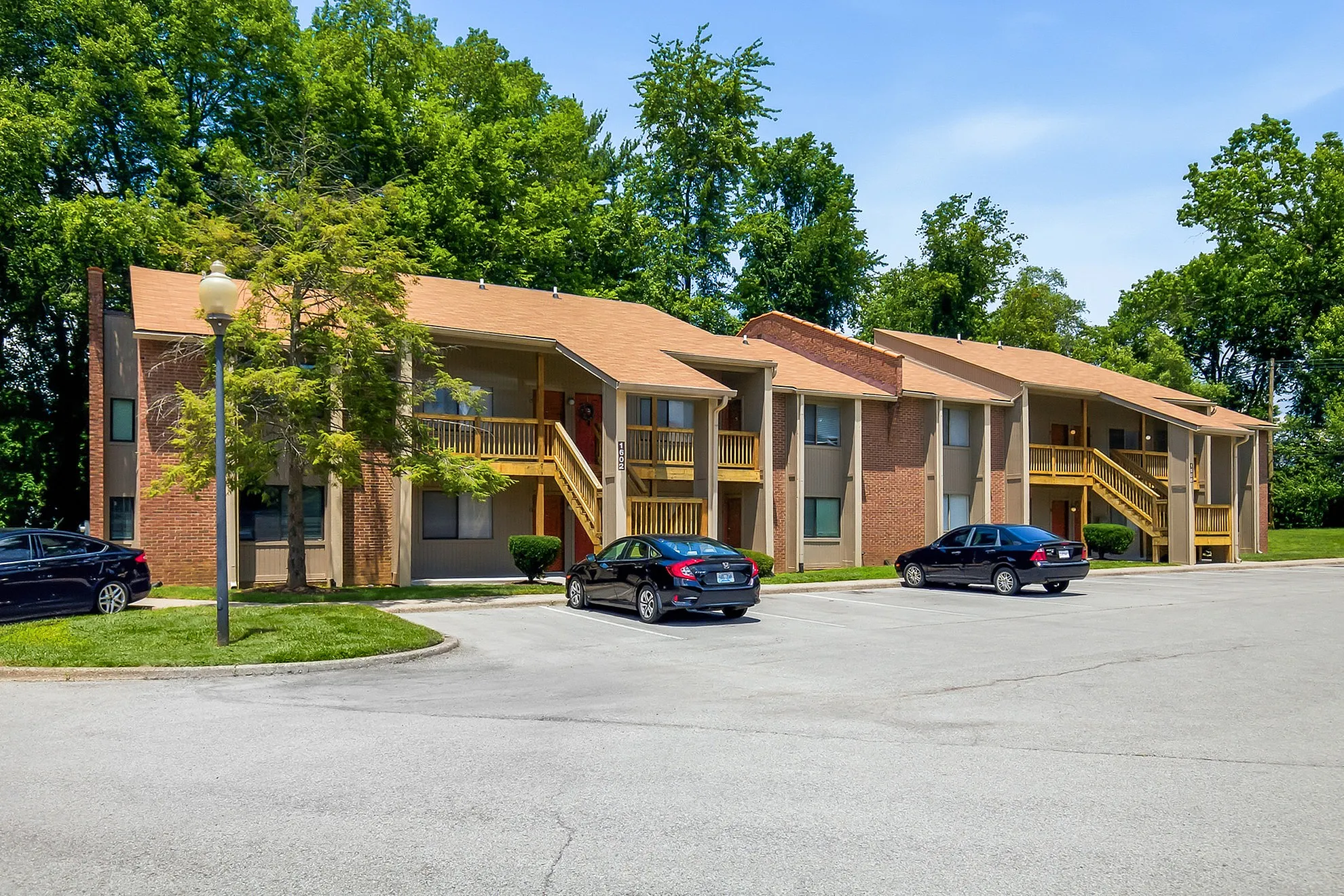 Charming brick apartment complex with balconies, nestled in lush greenery and ample parking space.