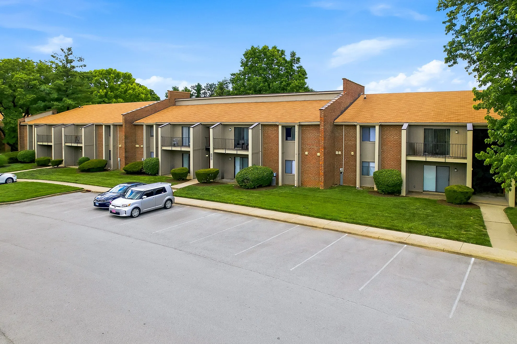 Charming apartment complex with modern architectural design and lush green surroundings, featuring ample parking space.