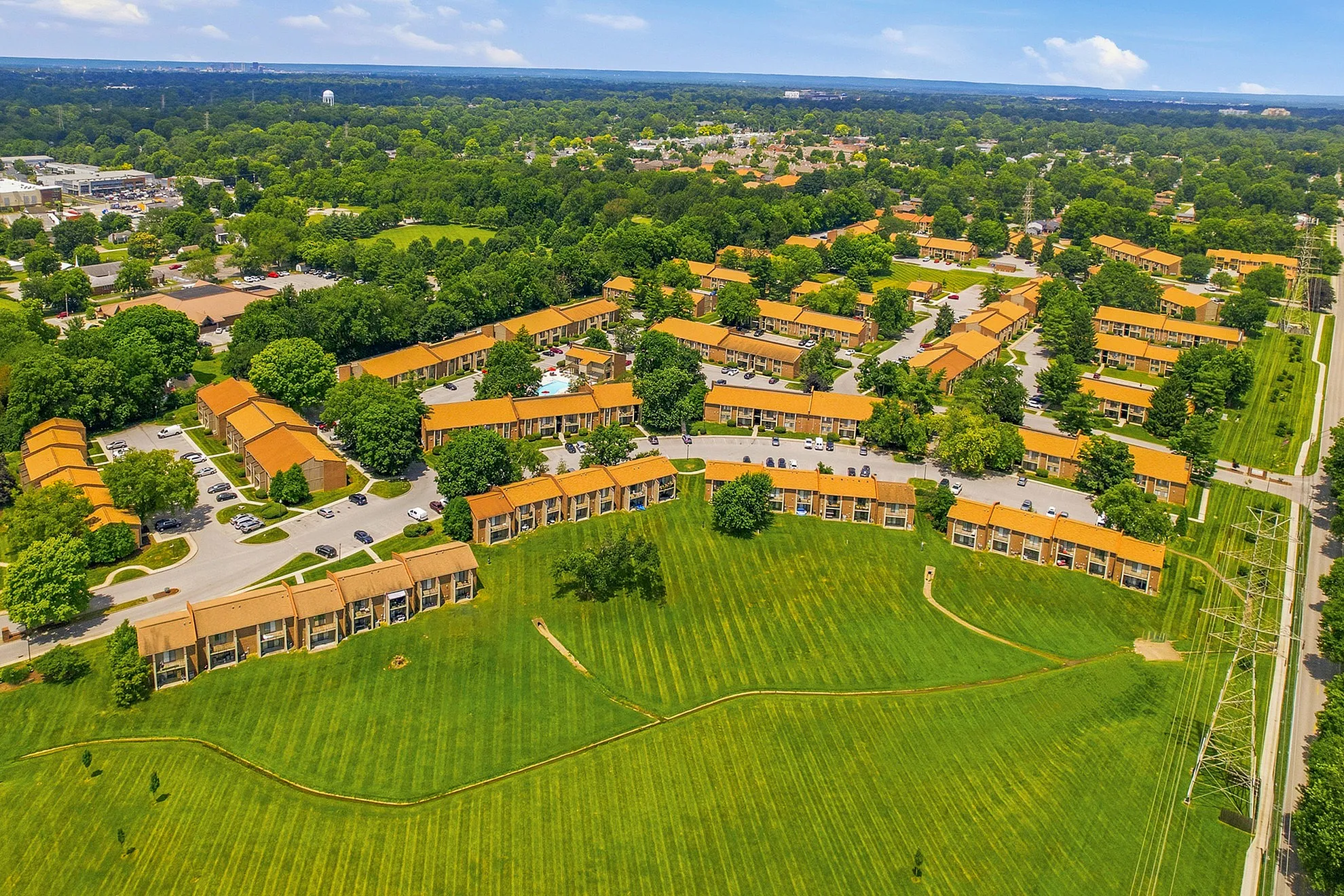 Vibrant aerial view of a beautifully landscaped apartment complex featuring cozy red-roofed buildings nestled in lush greenery, with a spacious park area perfect for relaxation.