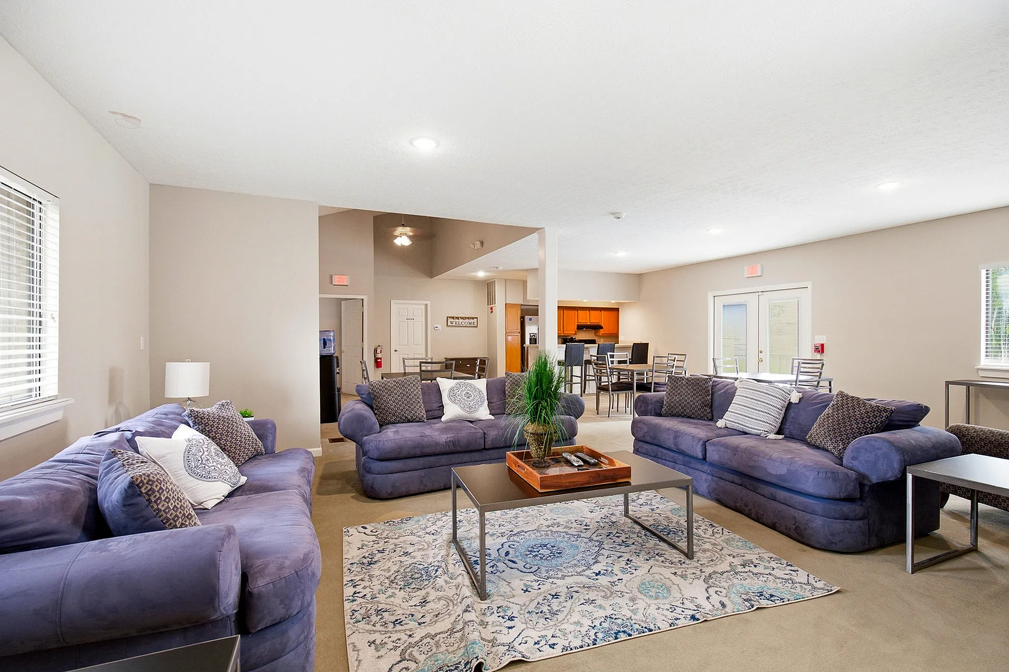 Elegant open-concept living area with plush blue sofas, stylish coffee table, and modern dining space in a bright, airy apartment.