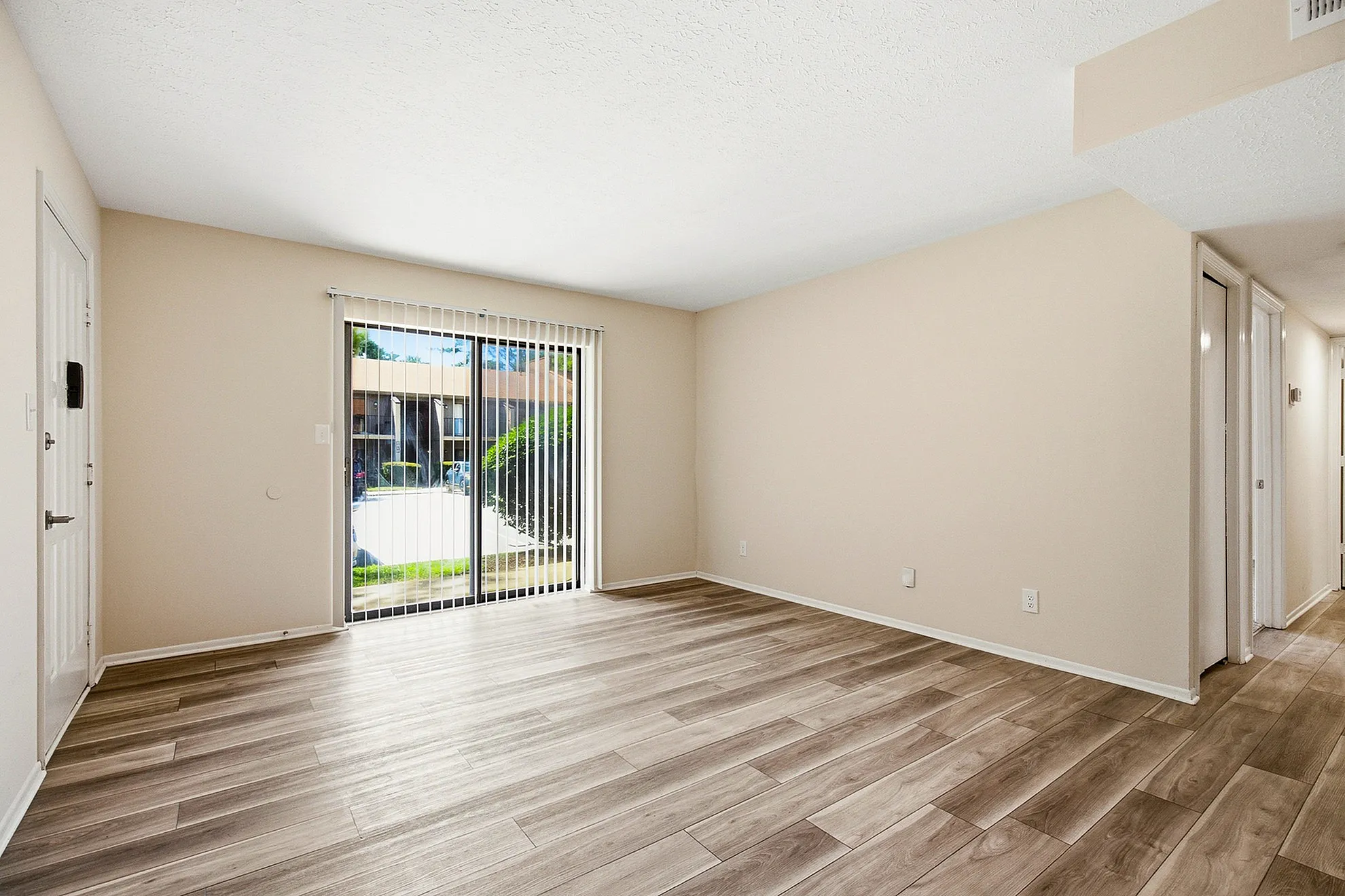 Bright and spacious living area with elegant wood flooring, large sliding doors leading to a scenic outdoor view, and ample natural light.